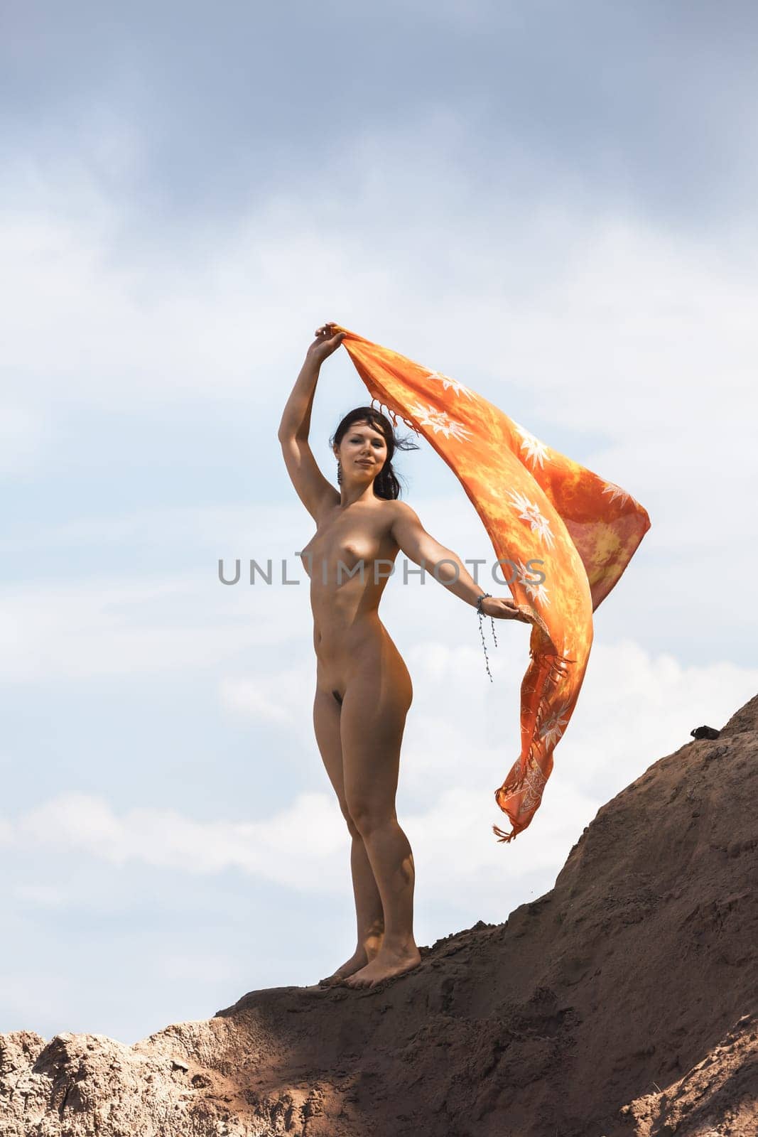 Young woman posing nude and enjoying nature on sand hill against sky background. Nature, beauty and nudity concept