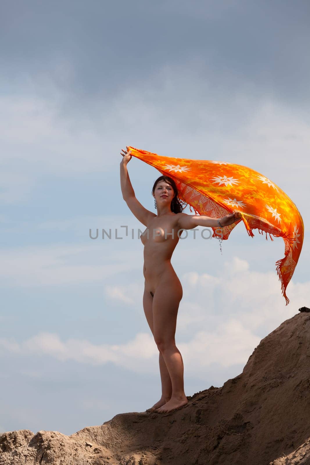 Young woman posing nude and enjoying nature on sand hill against sky background. Nature, beauty and nudity concept