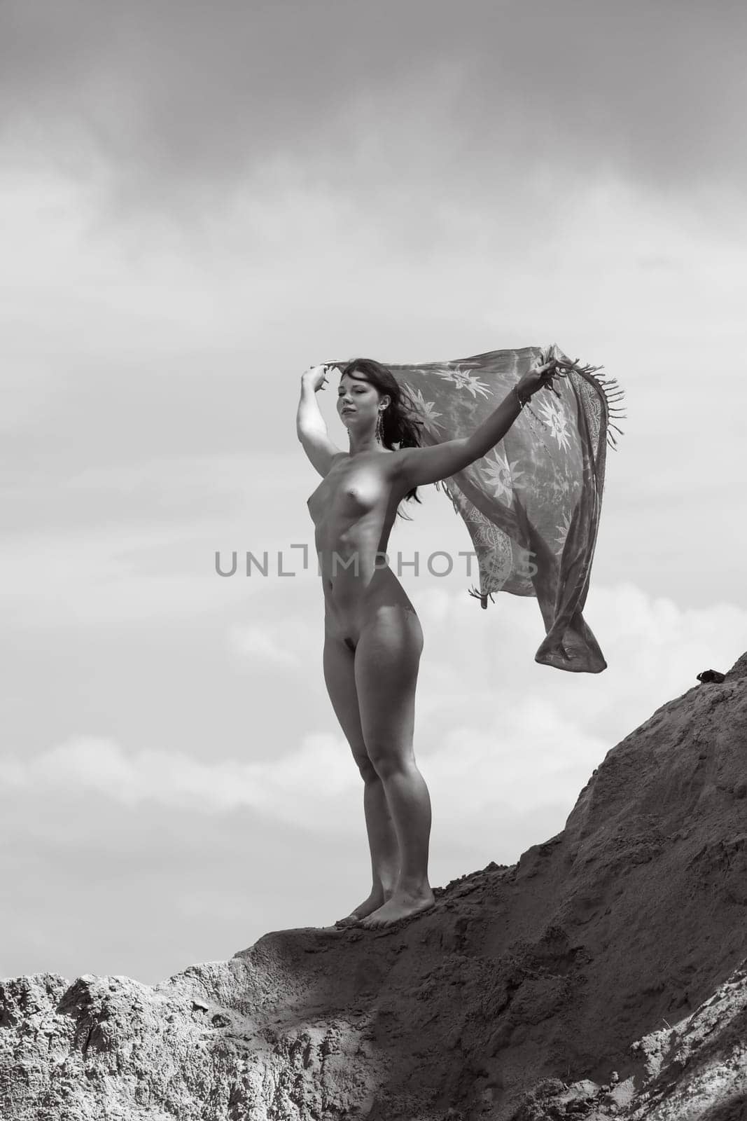 Young woman posing nude and enjoying nature on sand hill against sky background. Nature, beauty and nudity concept