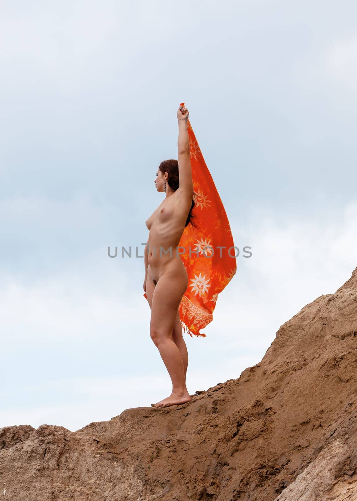 Young woman posing nude and enjoying nature on sand hill against sky background. Nature, beauty and nudity concept