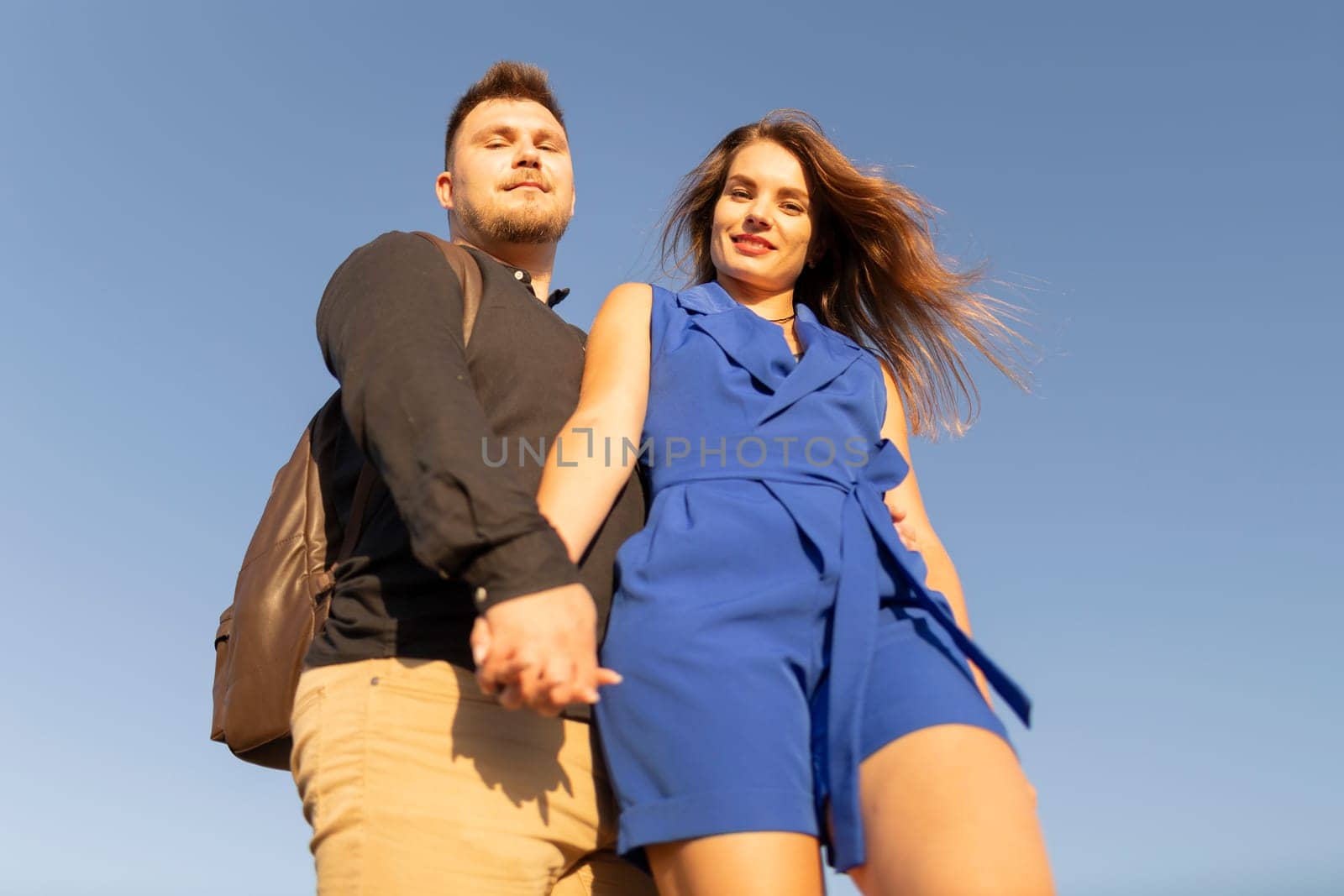 Young couple holding hands is standing under a blue sky on a sunny summer day
