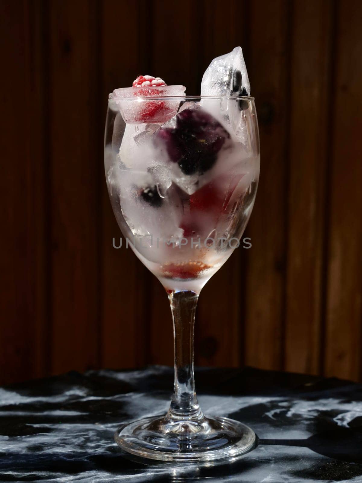 Glass with ice cubes with frozen berries and fruits close-up for a refreshing drink and preservation of seasonal vitamins raspberries, strawberries, cherries, blueberries, mulberries, blackberries