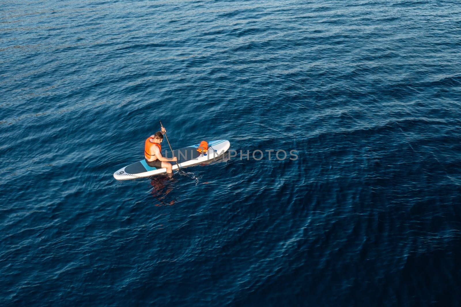 A male tourist, surrounded by the breathtaking blue of the azure sea, paddles effortlessly on a board