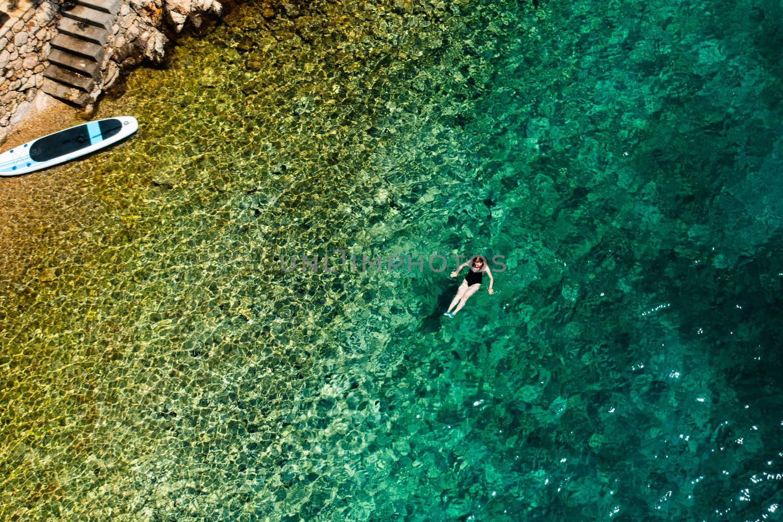 Woman swimming on the back in crystal clear water and paddle board is on the seaside.