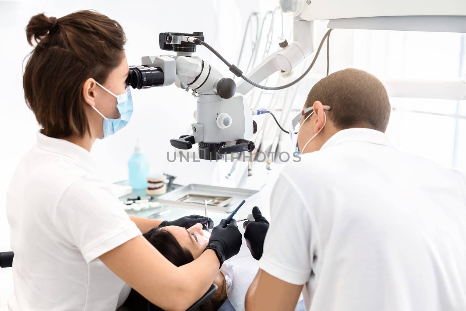 Difficult cases in stomatology. Back view of two dentists making treatment in modern dental office