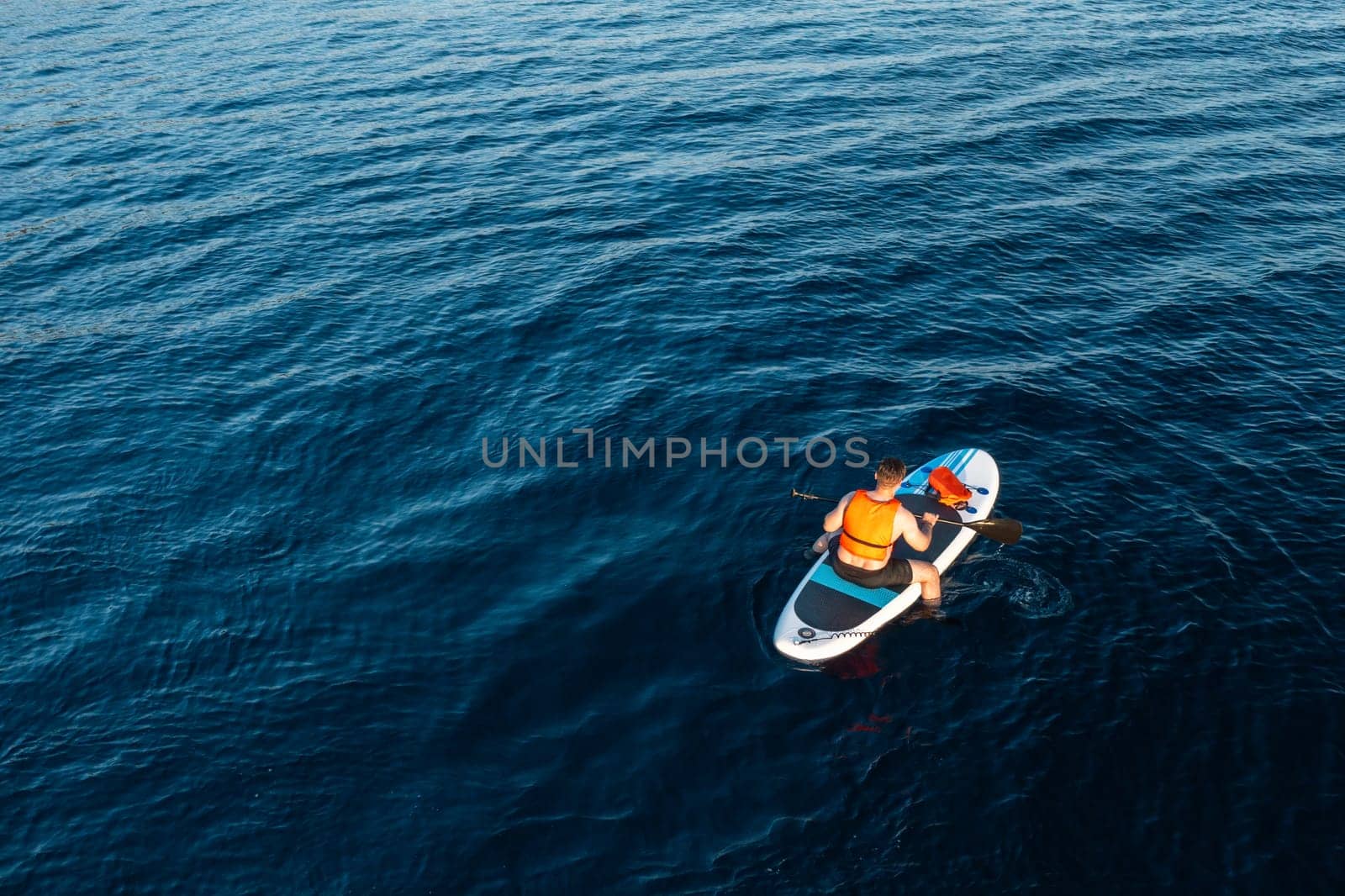 Aerial view of man sitting on the SUP surrounded by the breathtaking blue of the azure sea