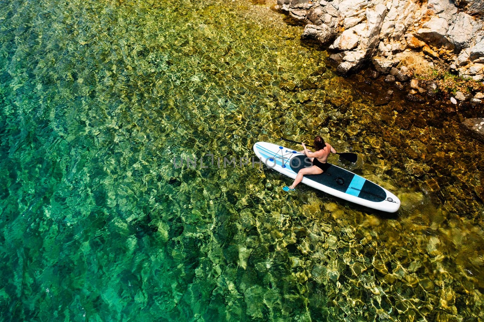 Woman moving on the paddle board close to the rocky seaside