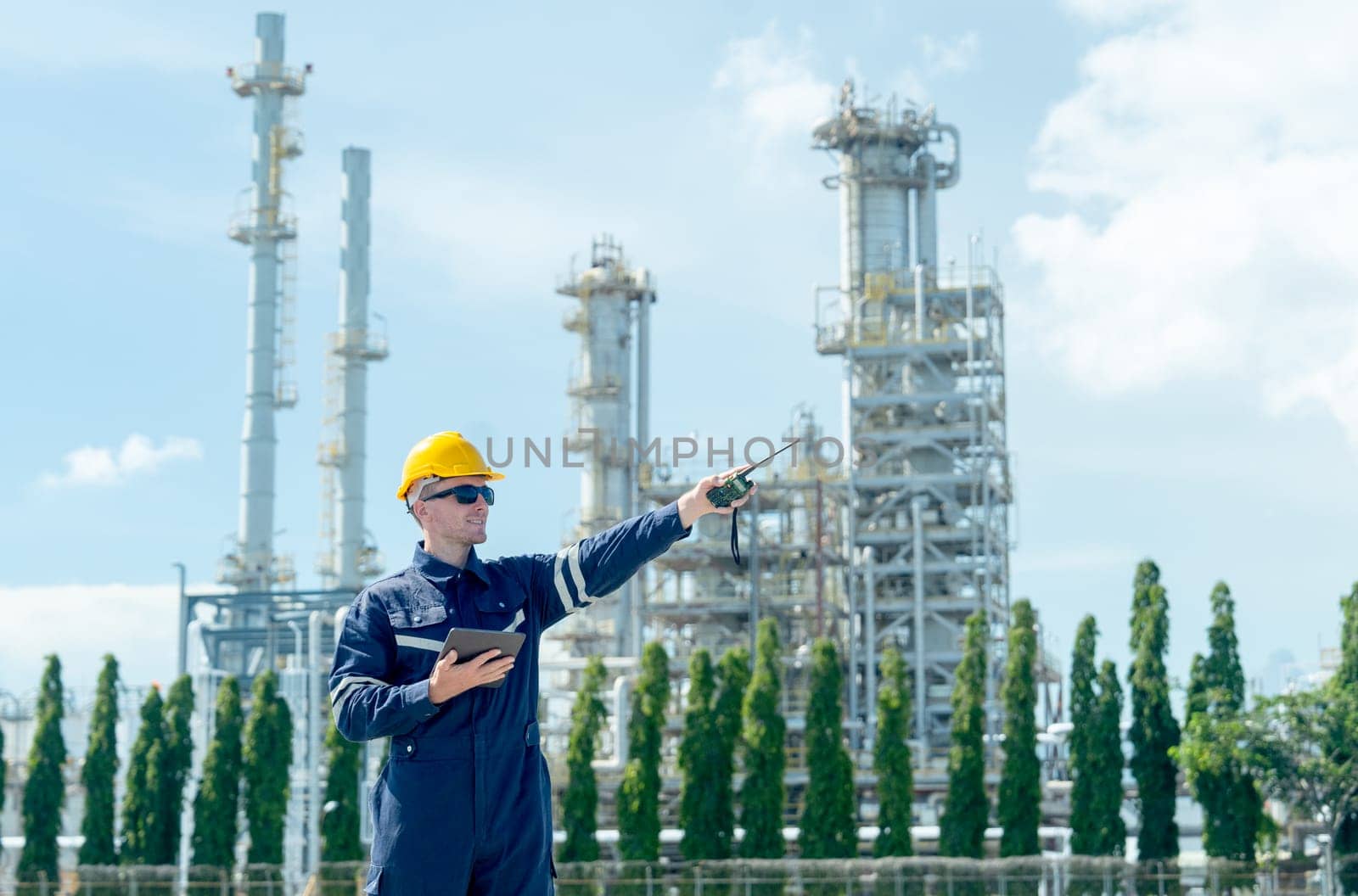 Factory engineer or technician worker man hold walkie-talkie and point to right side stand in front of  refining and petrochemical factory with day light.