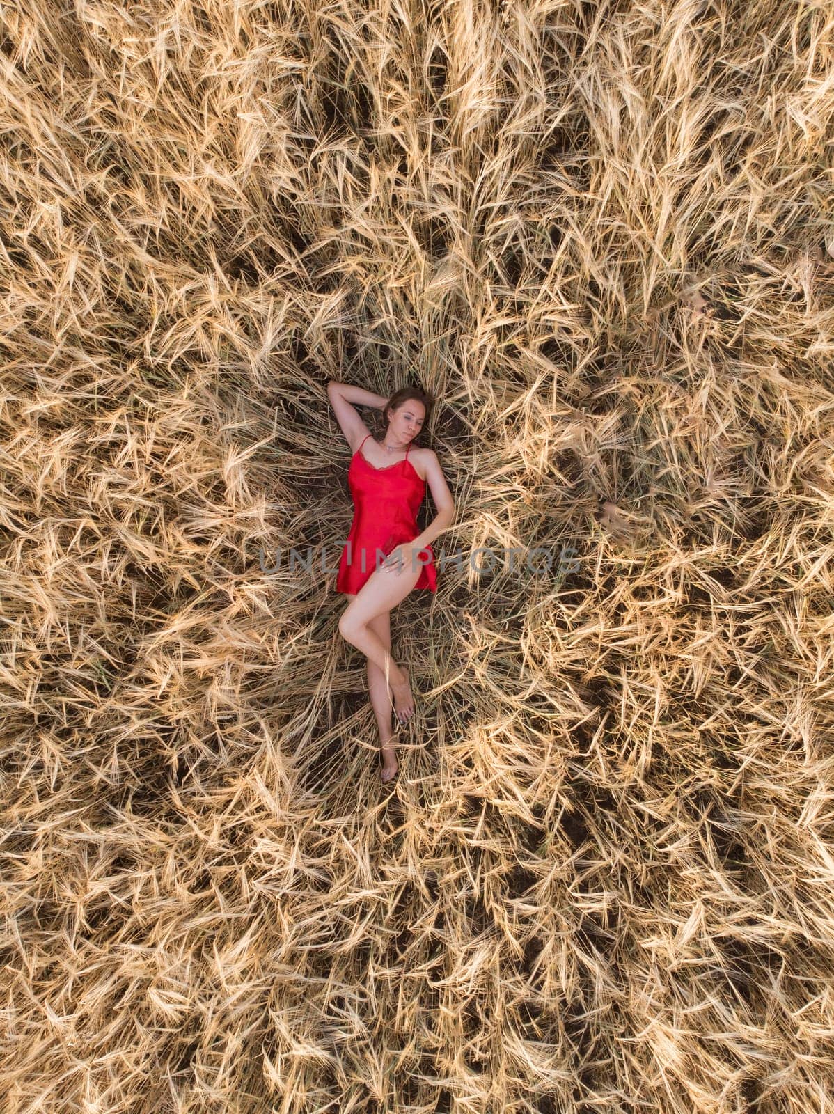 Aerial view of woman in red dress lying in the yellow field of wheat