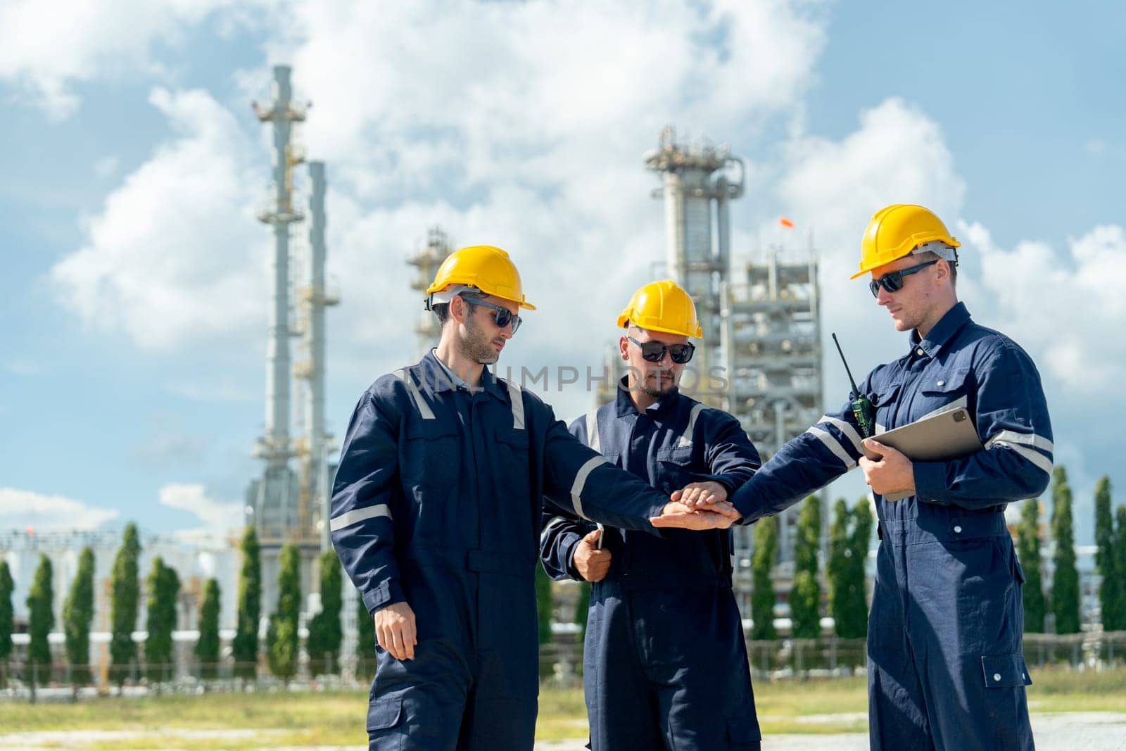 Wide shot of factory engineer or technician workers stand and join hands together in front of refining and petrochemical factory with day light.