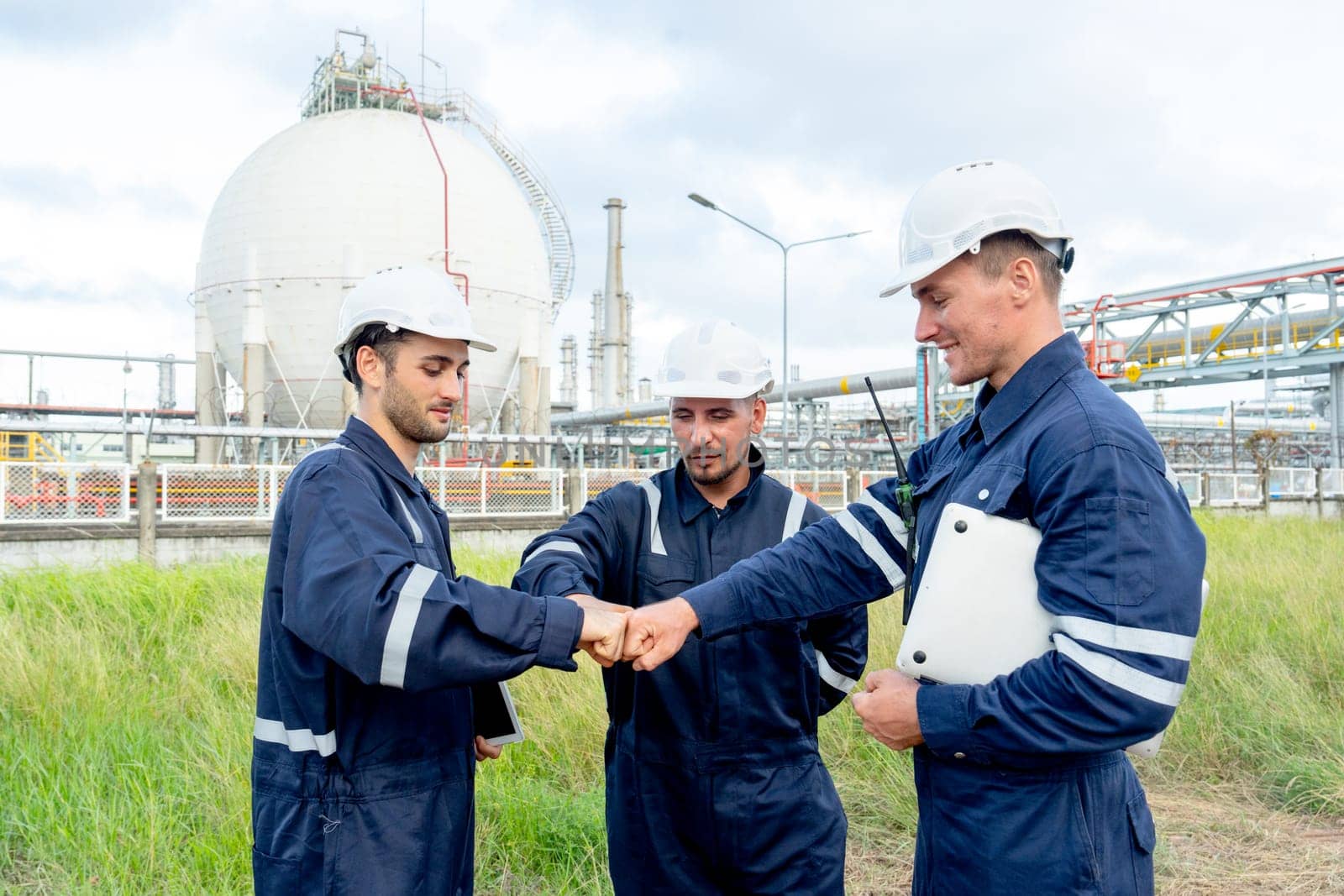 Group of engineer or technician workers stand in front of tank in petrochemical factory and they action of first bump.