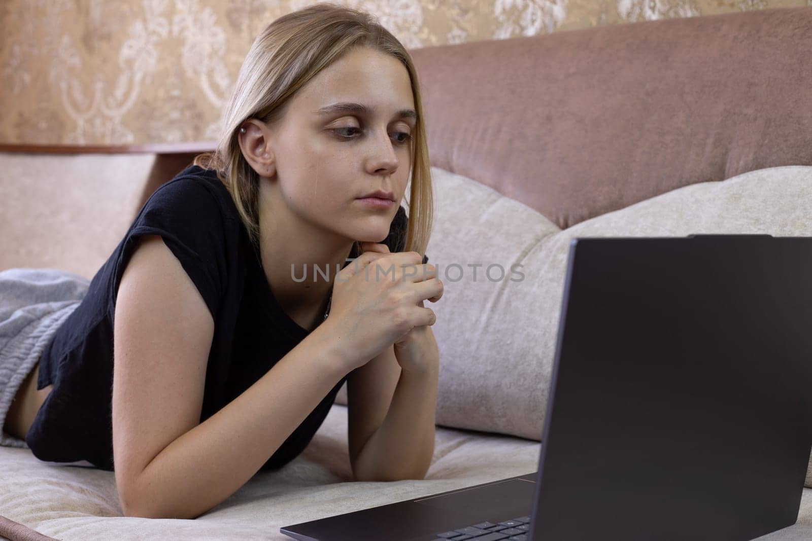 Girl student lies on sofa on her stomach and uses laptop while listening to webinar, distance modern learning of the future generation