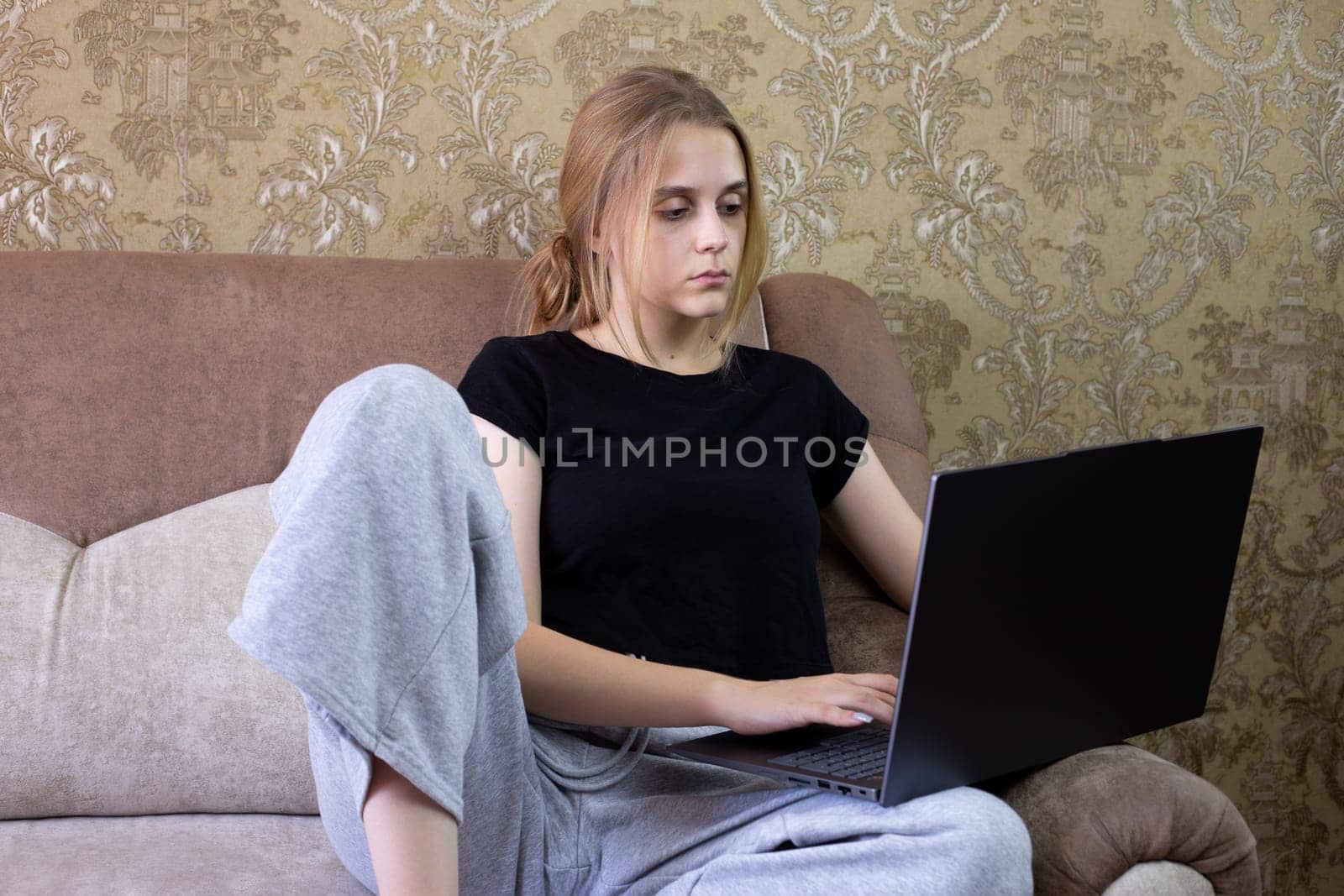 Young woman is engaged in remote work on her laptop while comfortably seated in a cozy living room space