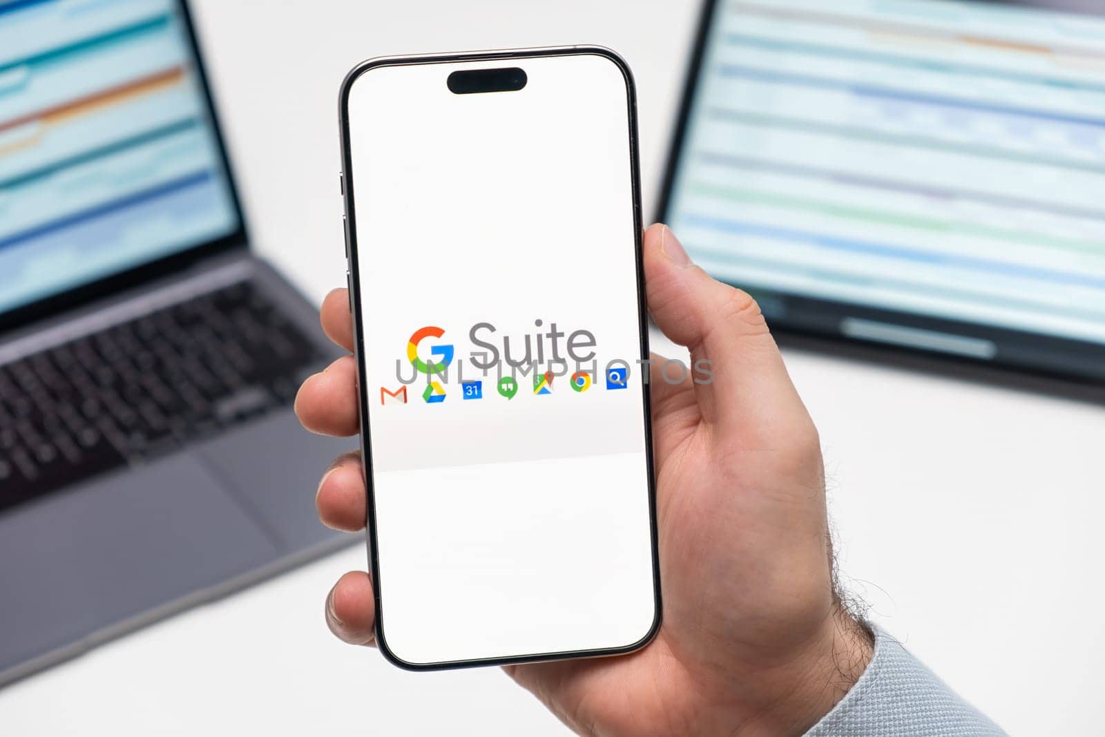 PRAGUE, CZECHIA - JULY, 2024: Google Suite logo on the screen of smartphone in mans hand and laptop on the background