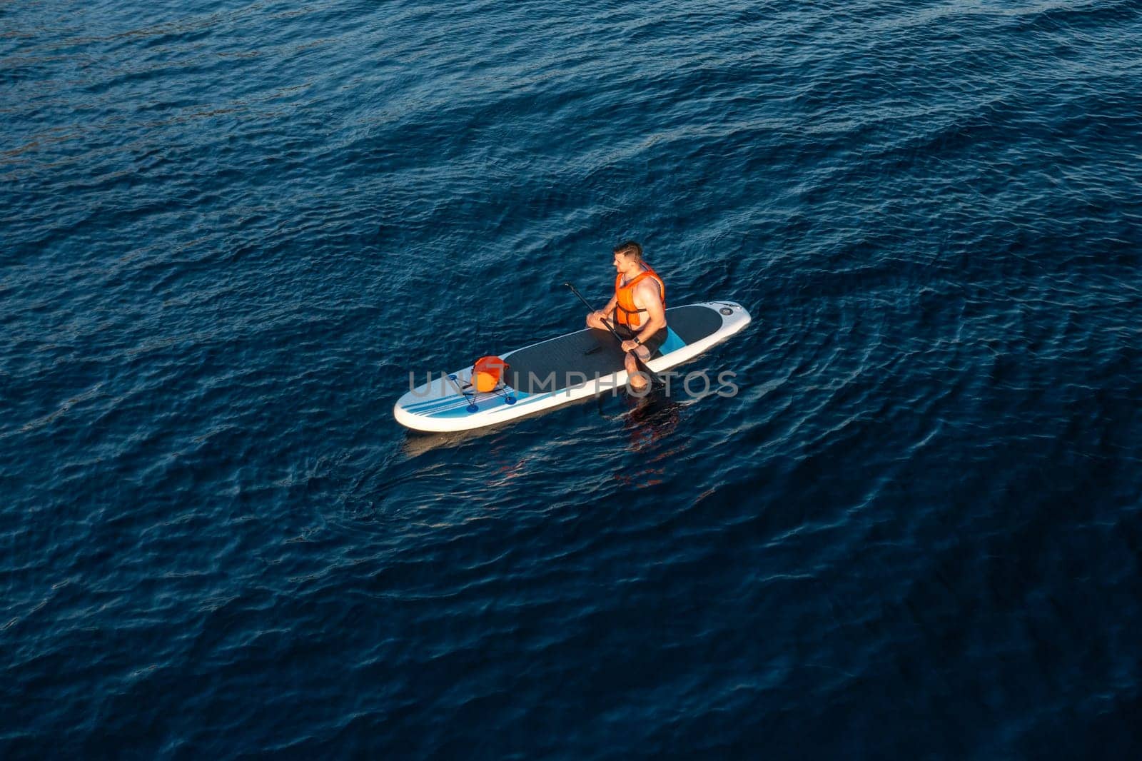 A tourist on a paddleboard enjoys the pristine beauty of the azure sea, aerial view