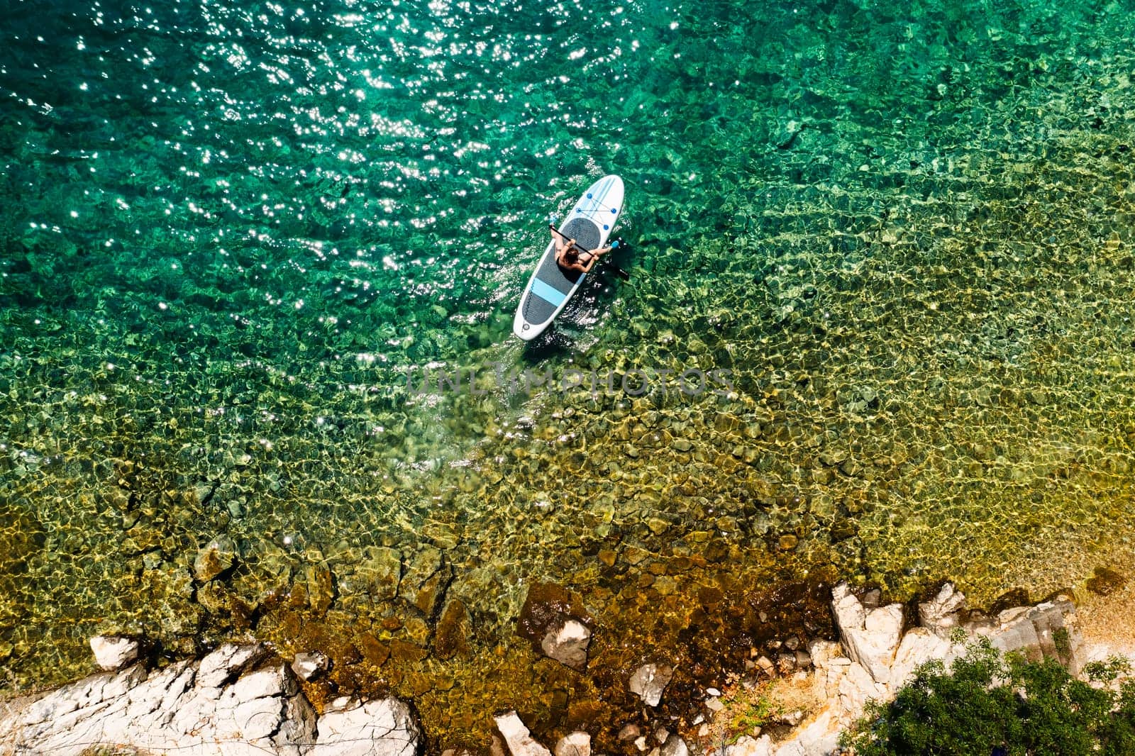 Top view of woman navigates SUP in the tranquil clear water.