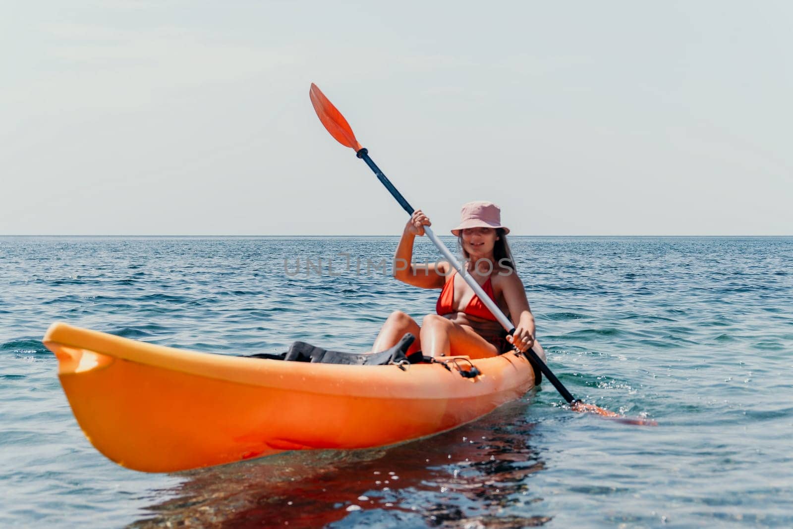 Happy smiling woman in kayak on ocean, paddling with wooden oar. Calm sea water and horizon in background