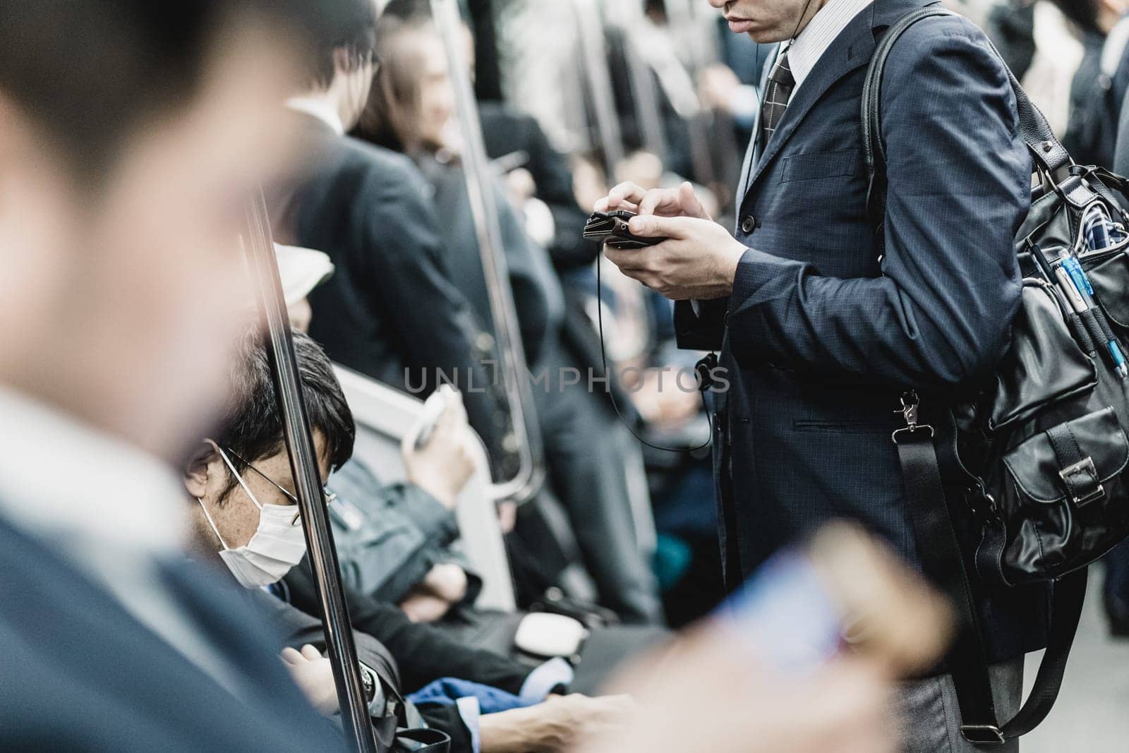 Interior of modern Tokyo metro with passengers on seats and businessmen using their cell phones. Corporate business people commuting to work by public transport. Horizontal composition.