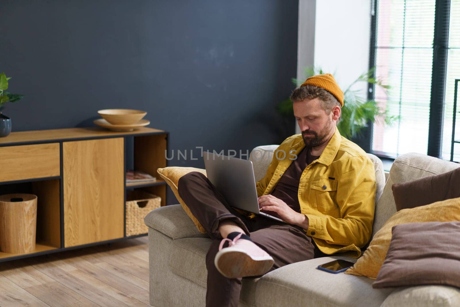 Tired man seeks solace on sofa home, battling exhaustion as engages with laptop, either in search of information or exploring websites on web. Modern digital age. High quality photo