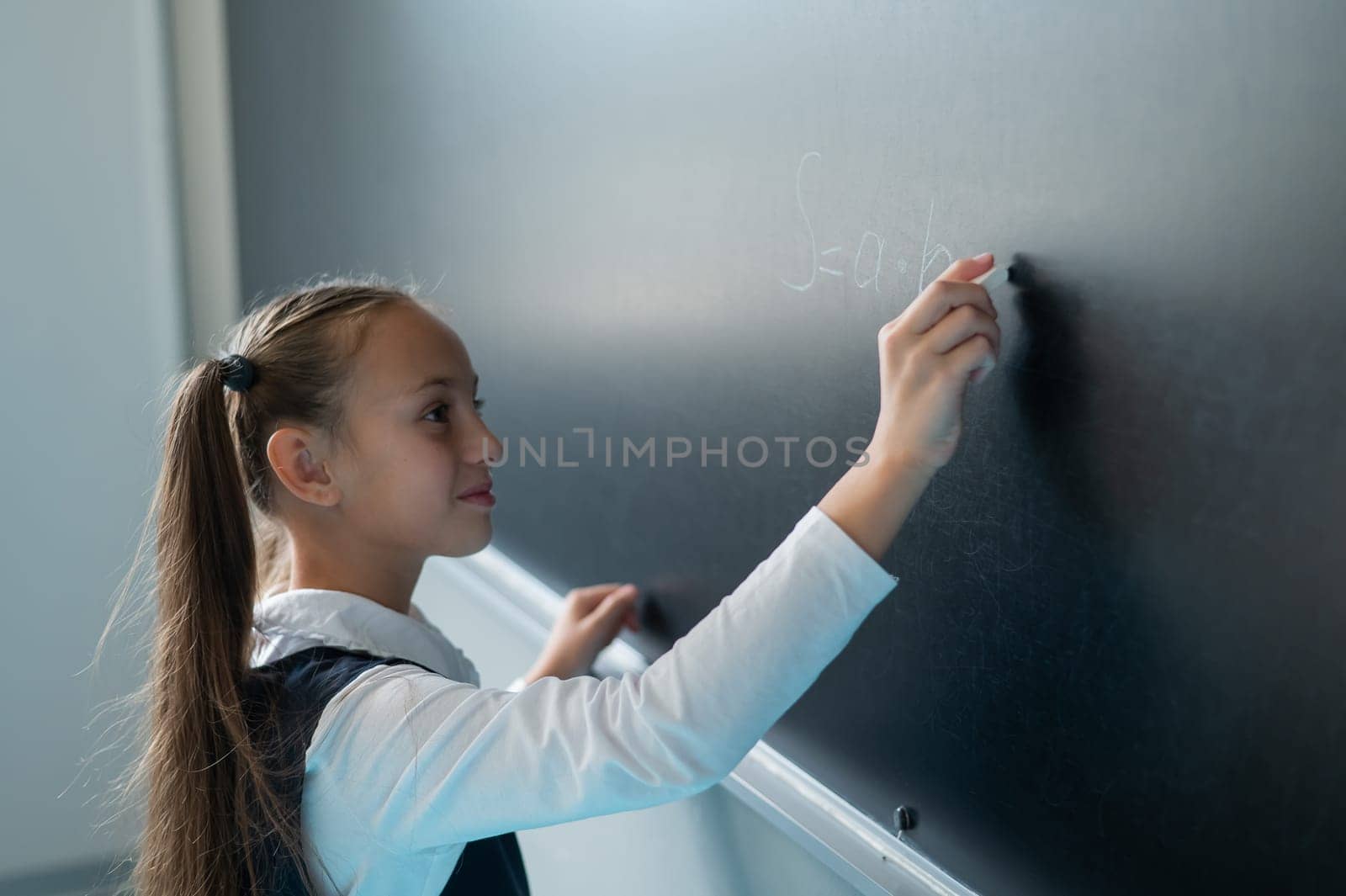 The schoolgirl answers at the lesson. Caucasian girl writes a formula on a blackboard