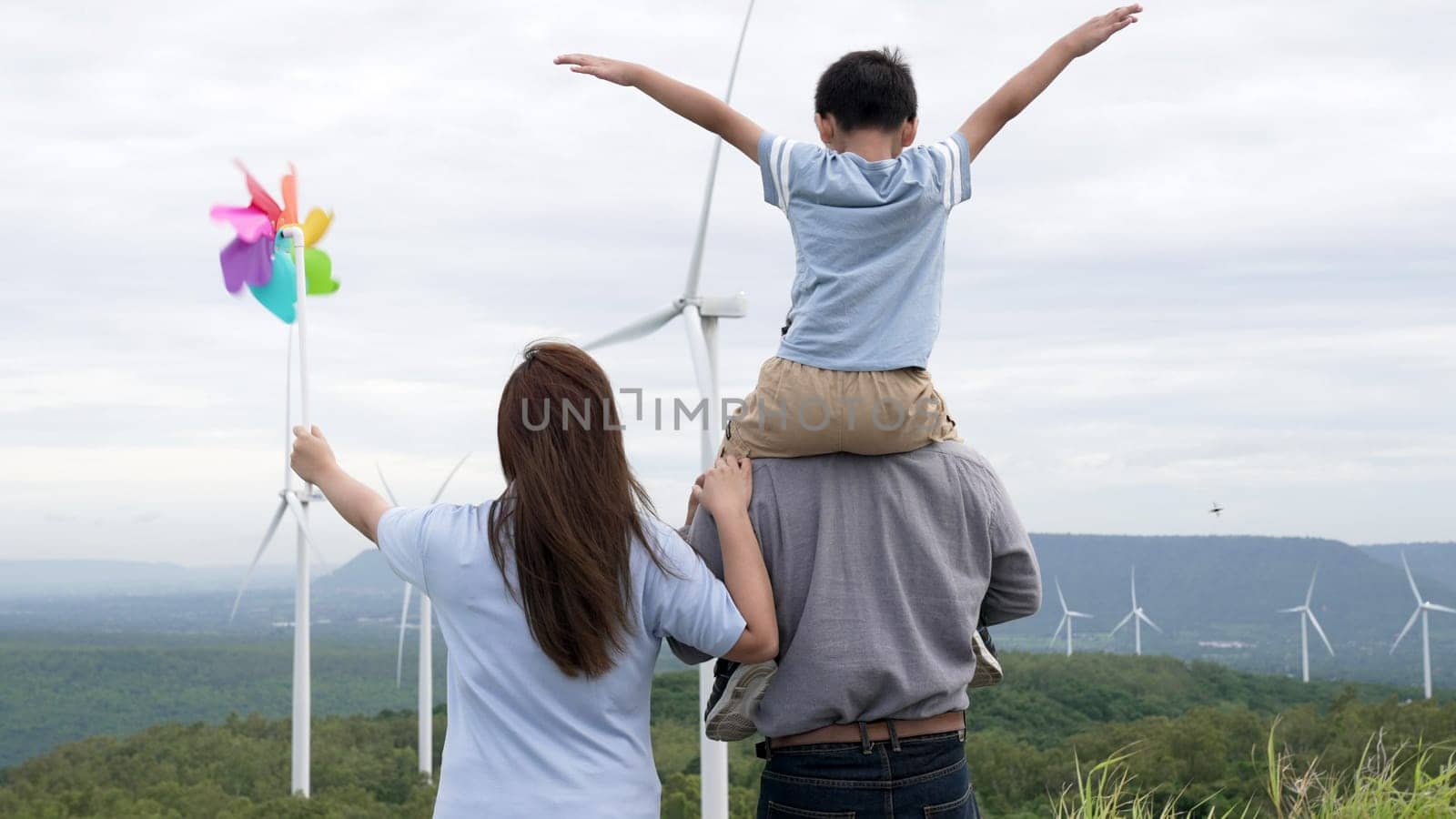 Concept of progressive happy family enjoying their time at the wind turbine farm. Electric generator from wind by wind turbine generator on the country side with hill and mountain on the horizon.