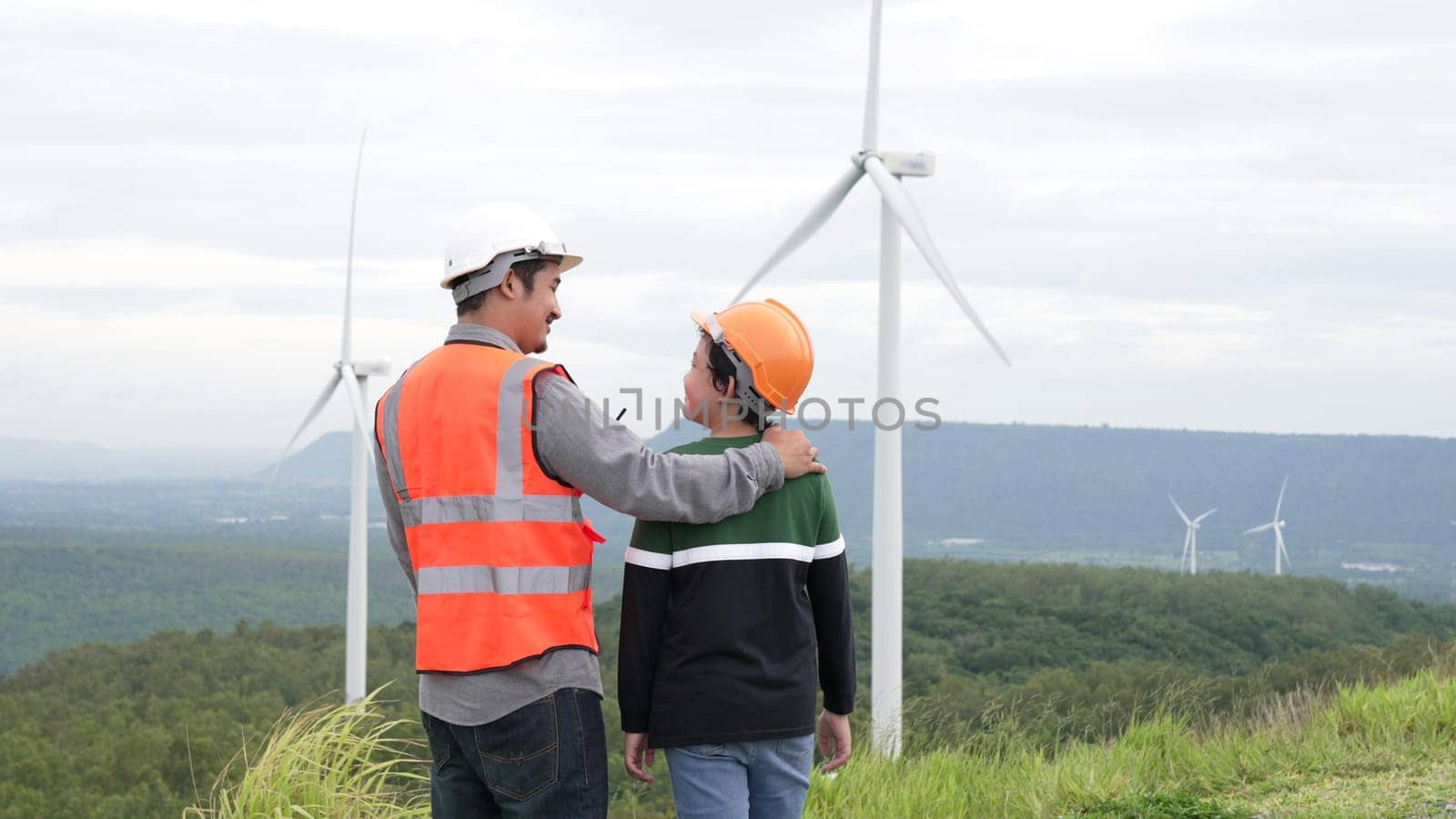 Engineer with his son on a wind farm atop a hill or mountain in the rural. Progressive ideal for the future production of renewable, sustainable energy. Energy generation from wind turbine.