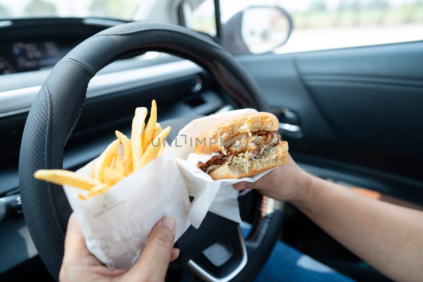 Asian lady holding hamburger and French fries to eat in car, dangerous and risk an accident.