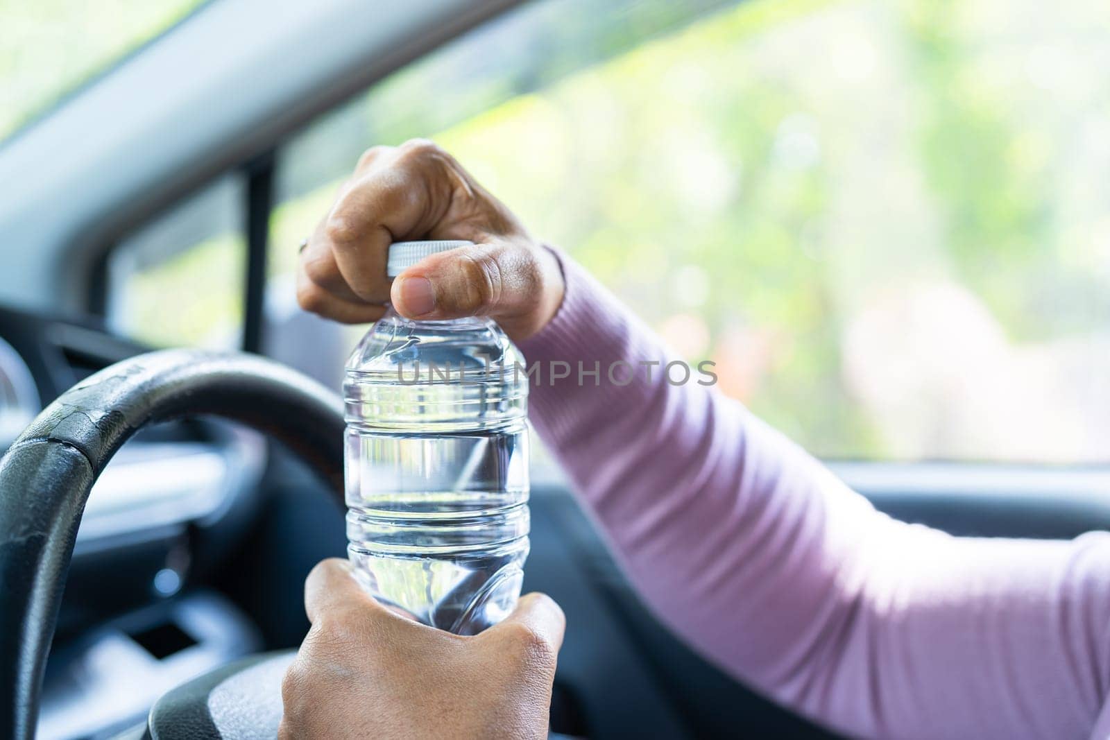 Asian woman driver holding bottle for drink water while driving a car. Plastic hot water bottle cause fire. by pamai