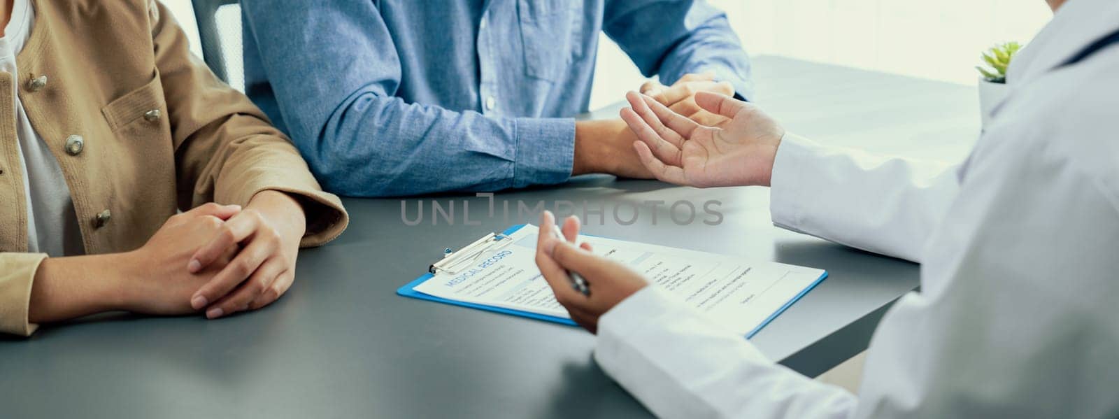 Doctor show medical diagnosis report and providing compassionate healthcare consultation to young couple patient in doctor clinic office. Doctor appointment and medical consult concept. Neoteric