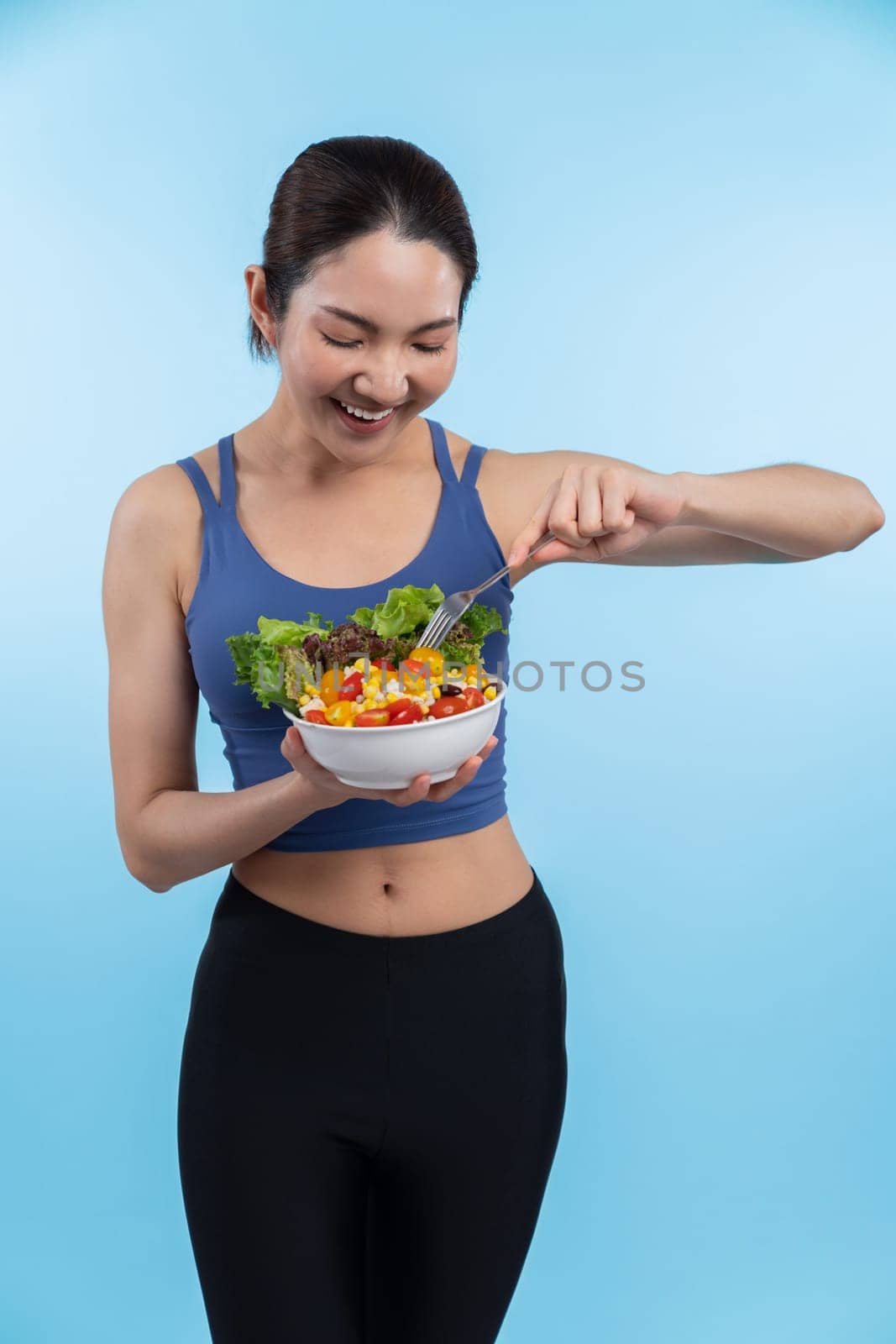 Young sporty Asian woman in sportswear holding salad bowl fill with vibrant of fruit and vegetable. Natural youthful and fit body lifestyle with balance nutrition on isolated background. Vigorous