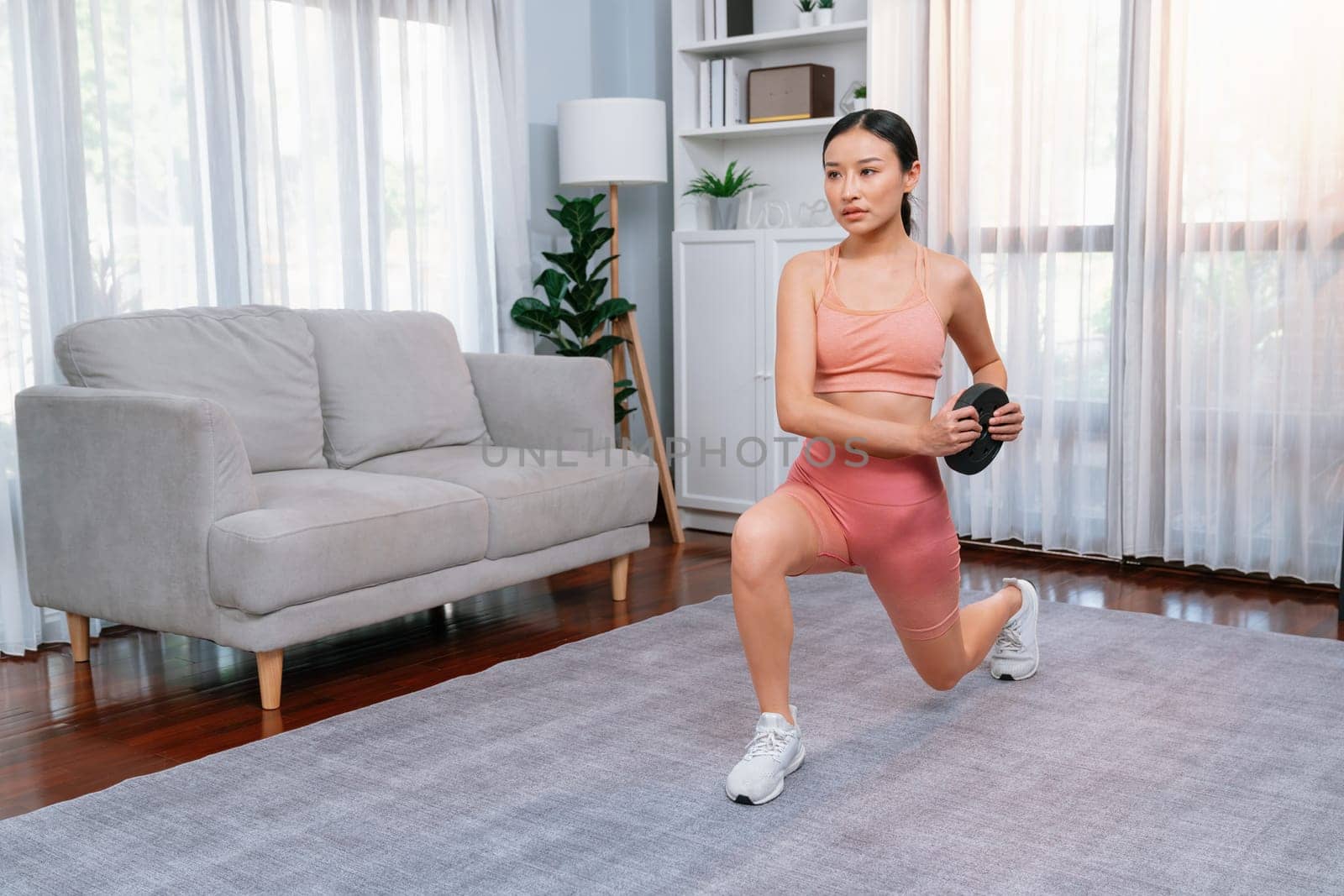 Vigorous energetic woman doing yoga and weight lifting exercise at home. Young athletic asian woman strength and endurance training session as home workout routine.