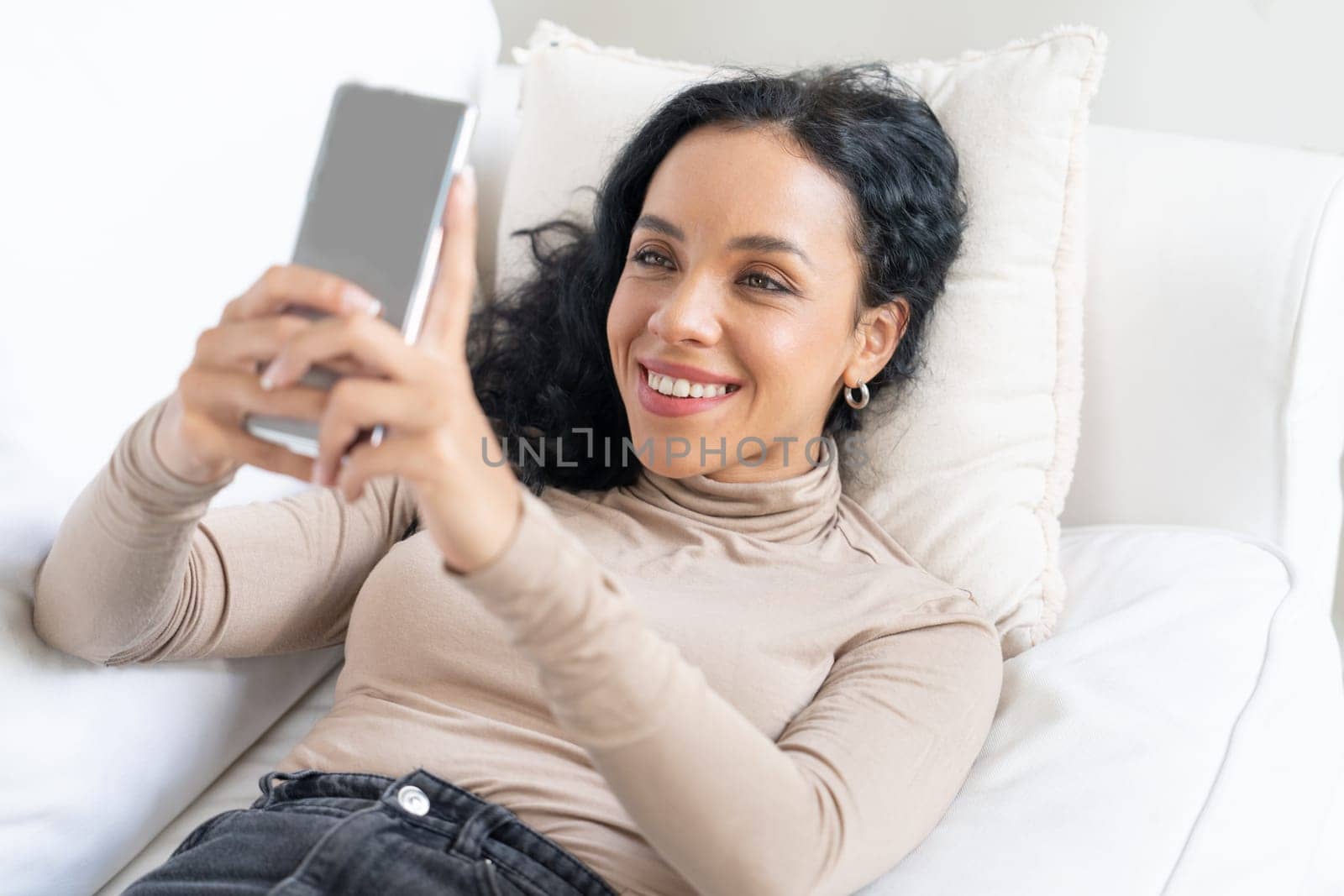 Relaxed young African American woman using crucial mobile phone on sofa couch in living room at home