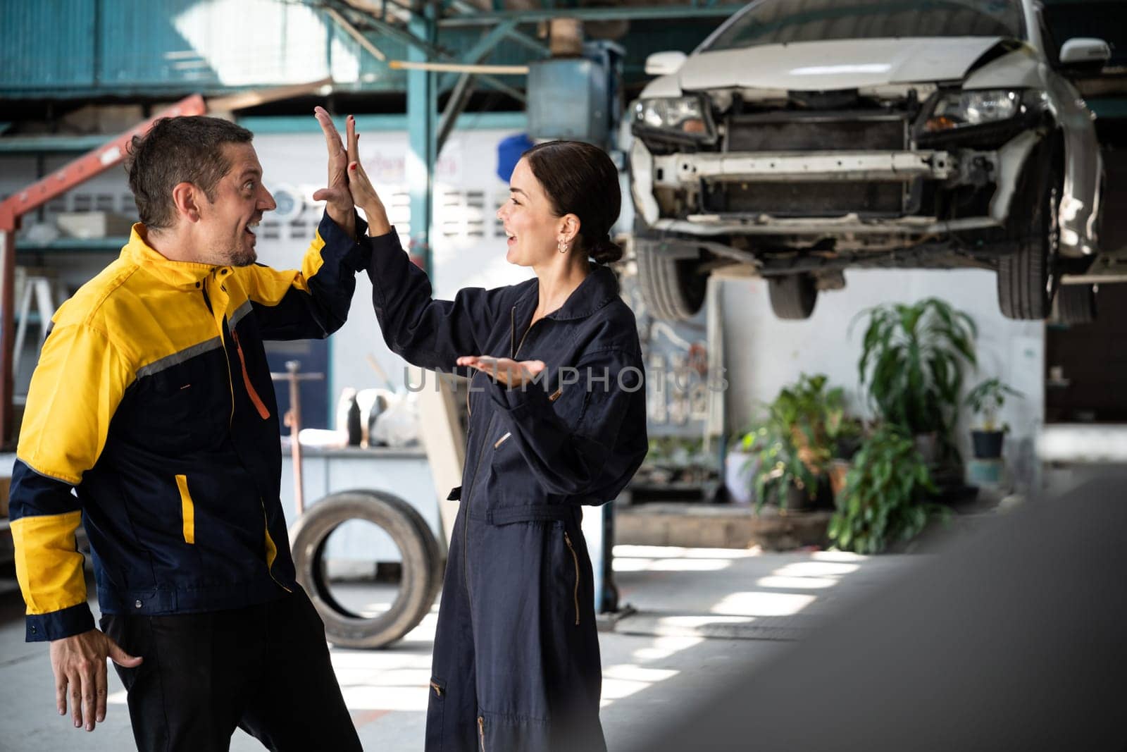 Two happy vehicle mechanic celebrate and high five after made successful car inspection or repair in automotive service car workshop. Technician team enjoy accomplishment together in garage. Oxus