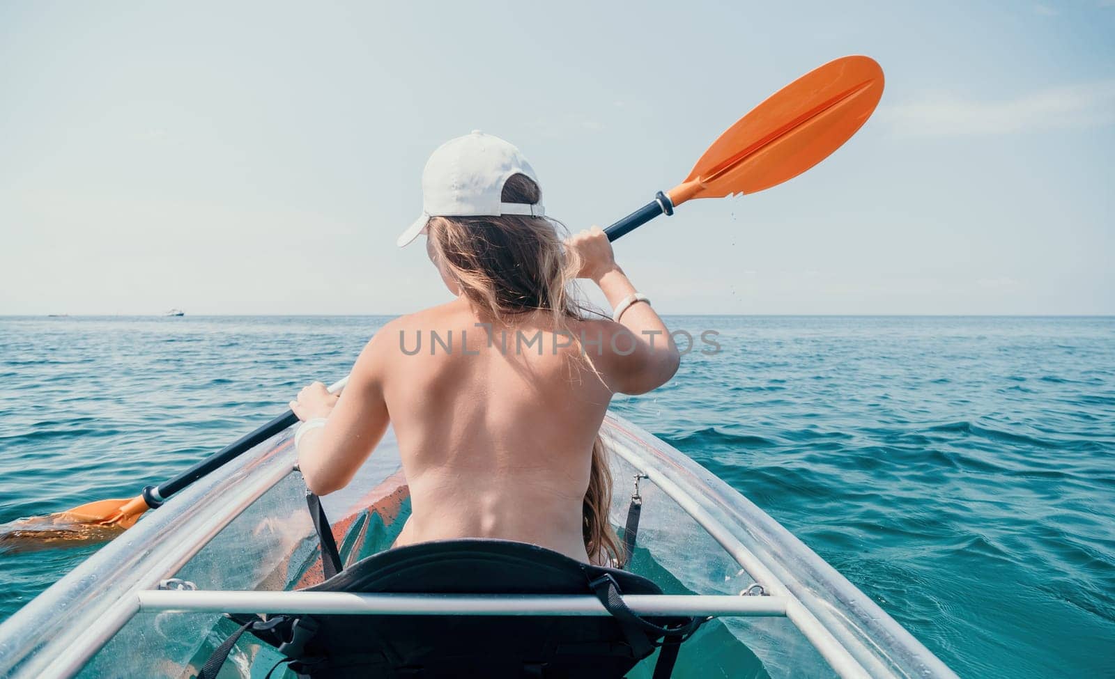 Woman in kayak back view. Happy young woman with long hair floating in transparent kayak on the crystal clear sea. Summer holiday vacation and cheerful female people relaxing having fun on the boat by panophotograph