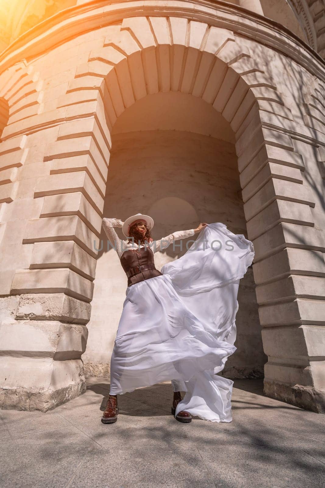 Stylish woman building city. A dancer in a long white skirt dances in front of a building with an arch. The skirt develops in the wind