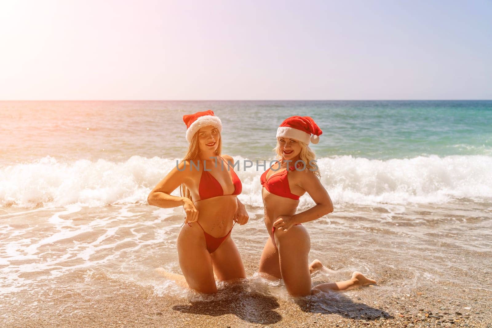 Women Santa hats ocean play. Seaside, beach daytime, enjoying beach fun. Two women in red swimsuits and Santa hats are enjoying themselves in the ocean waves