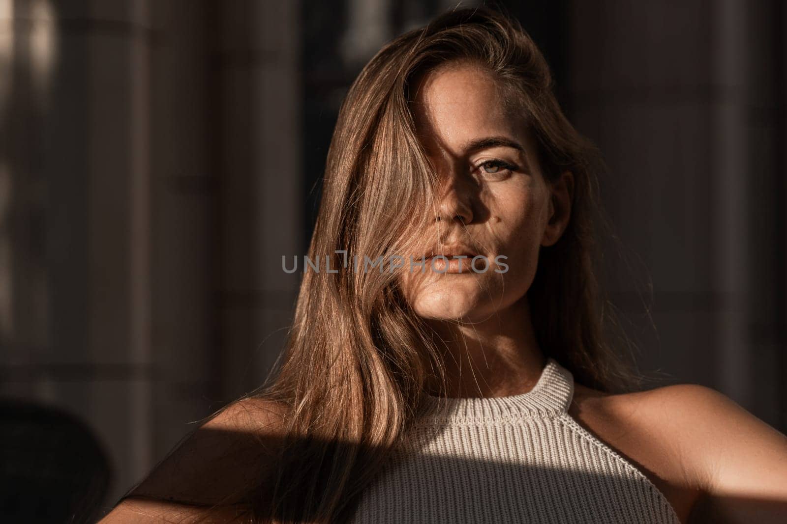 A woman with long brown hair looks intensely at the camera, her face partially obscured by her hair. The light casts a shadow across her face and body.