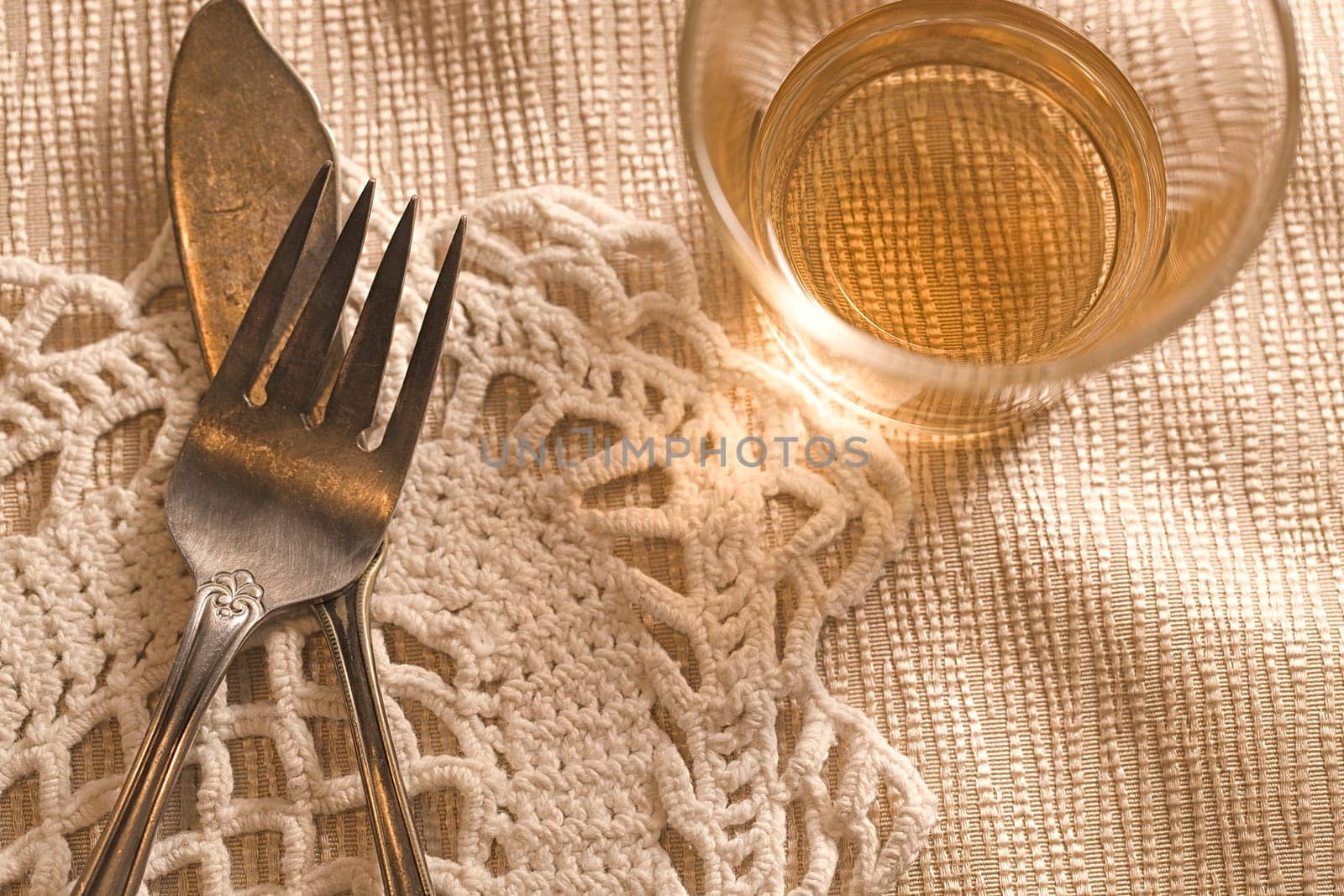 A concept photo of old tarnished fork and butter knife on the table with a mostly empty glass.
