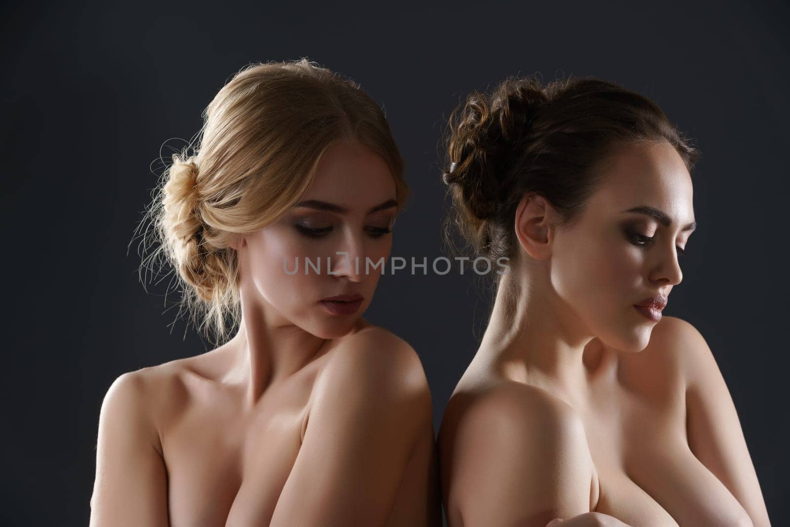 Two beautiful models with fine haistyles and make up posing together topless studio shot