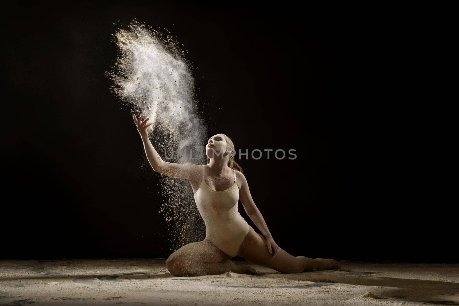 Young sexy gymnast in a cloud of white dust studio shot
