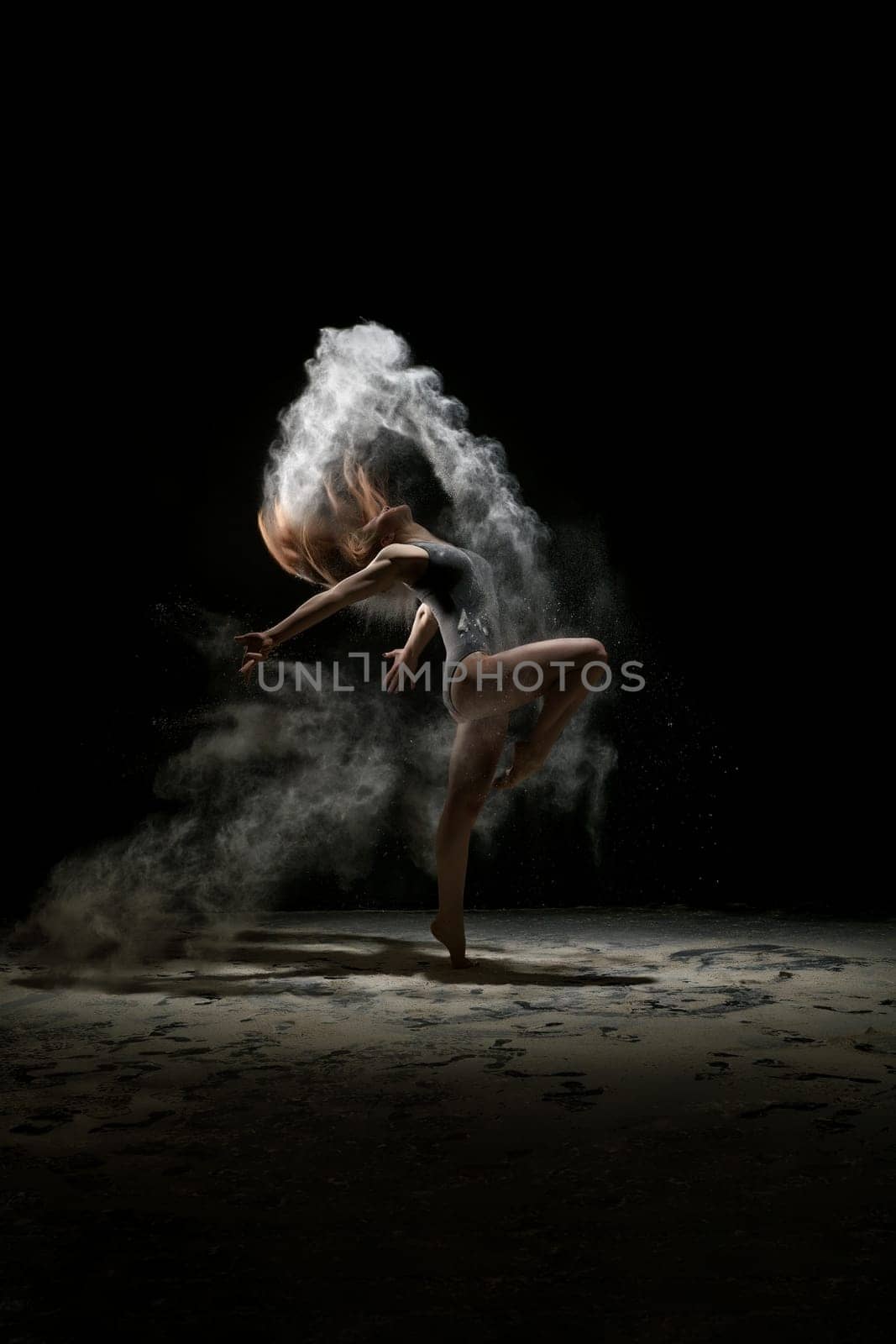 Young model dancing in a cloud of white dust studio shot