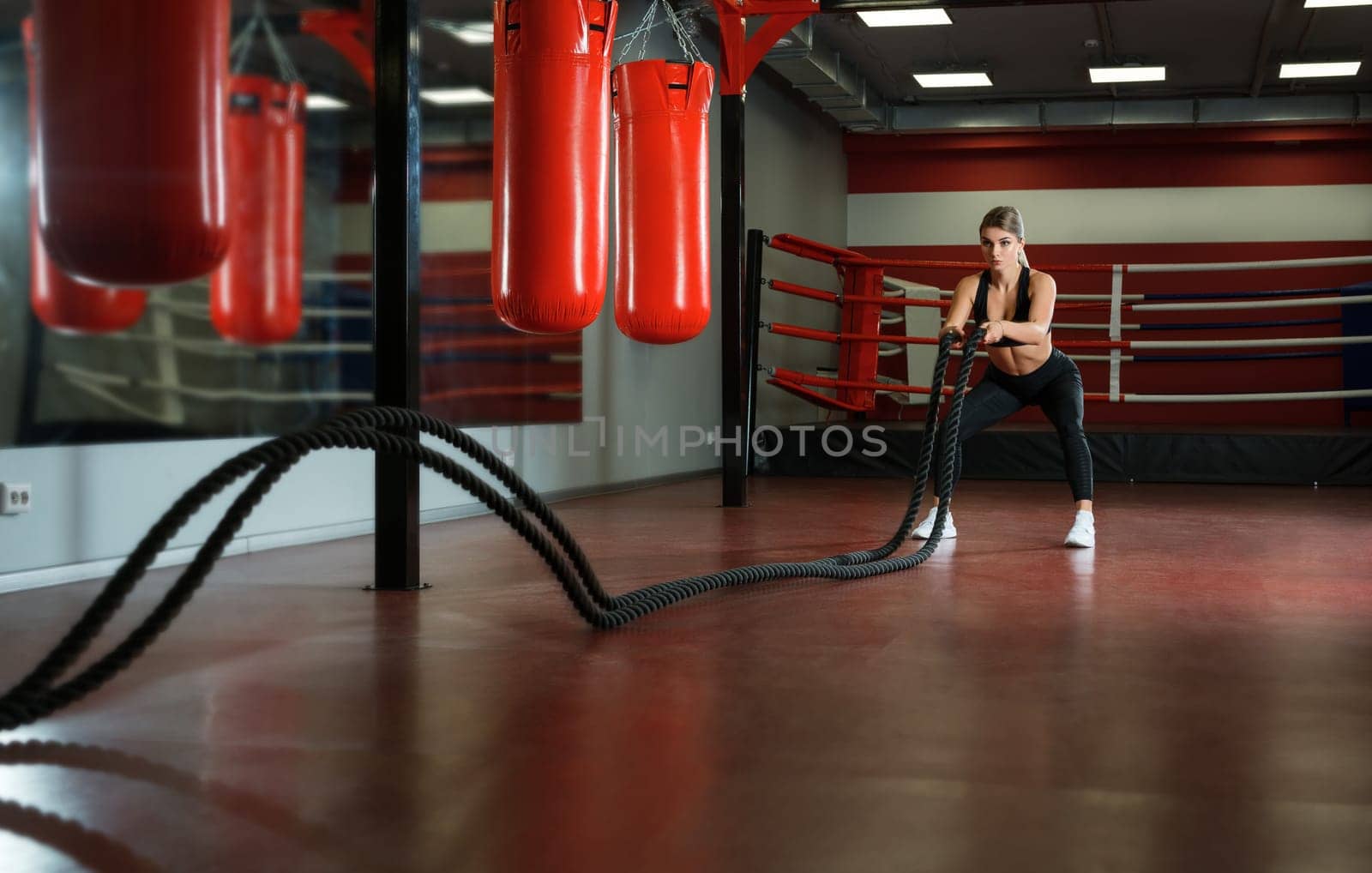 Sexy girl training in a gym with a rope boxing ring and punching bags on a background