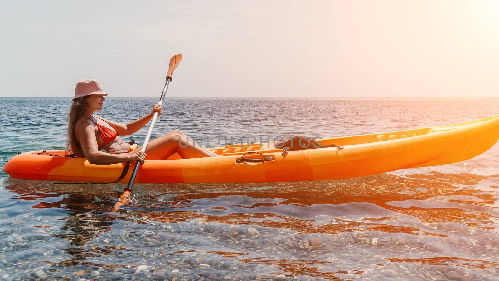 Happy smiling woman in kayak on ocean, paddling with wooden oar. Calm sea water and horizon in background