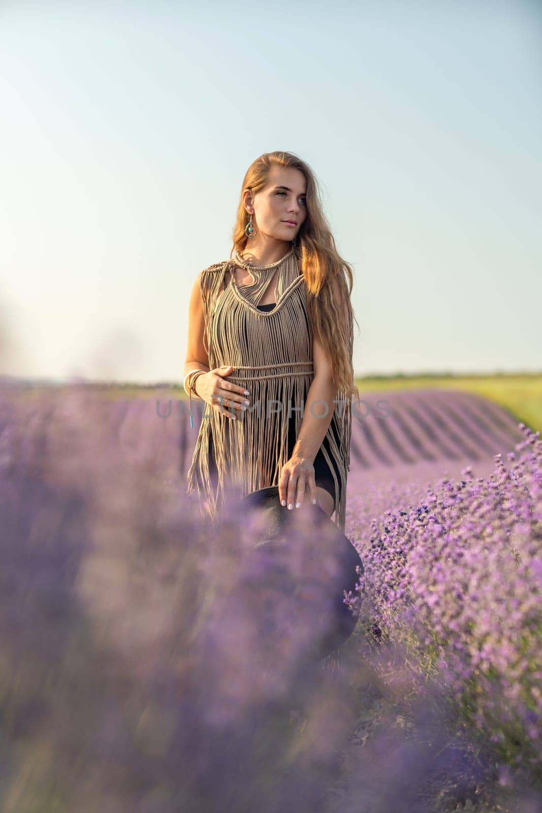 A woman is standing in a field of purple flowers, wearing a black dress and a black hat