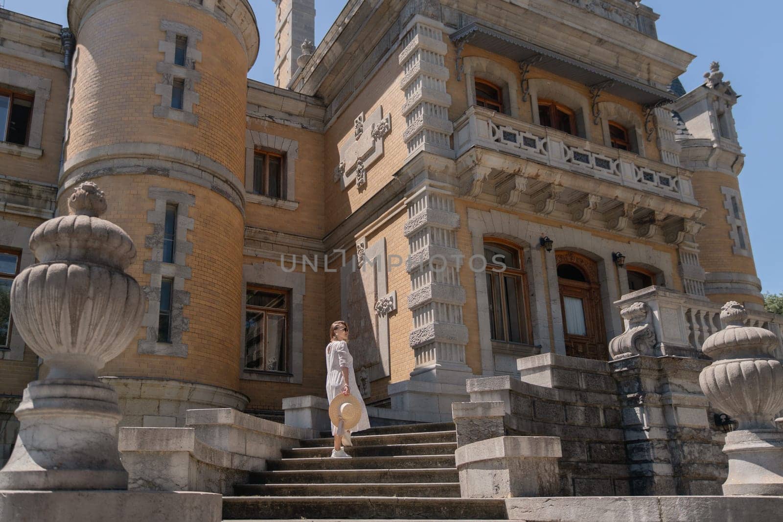 A woman is standing on a set of stairs in front of a large building. The building has a lot of architectural details, including a large archway and a balcony. The woman is wearing a white shirt