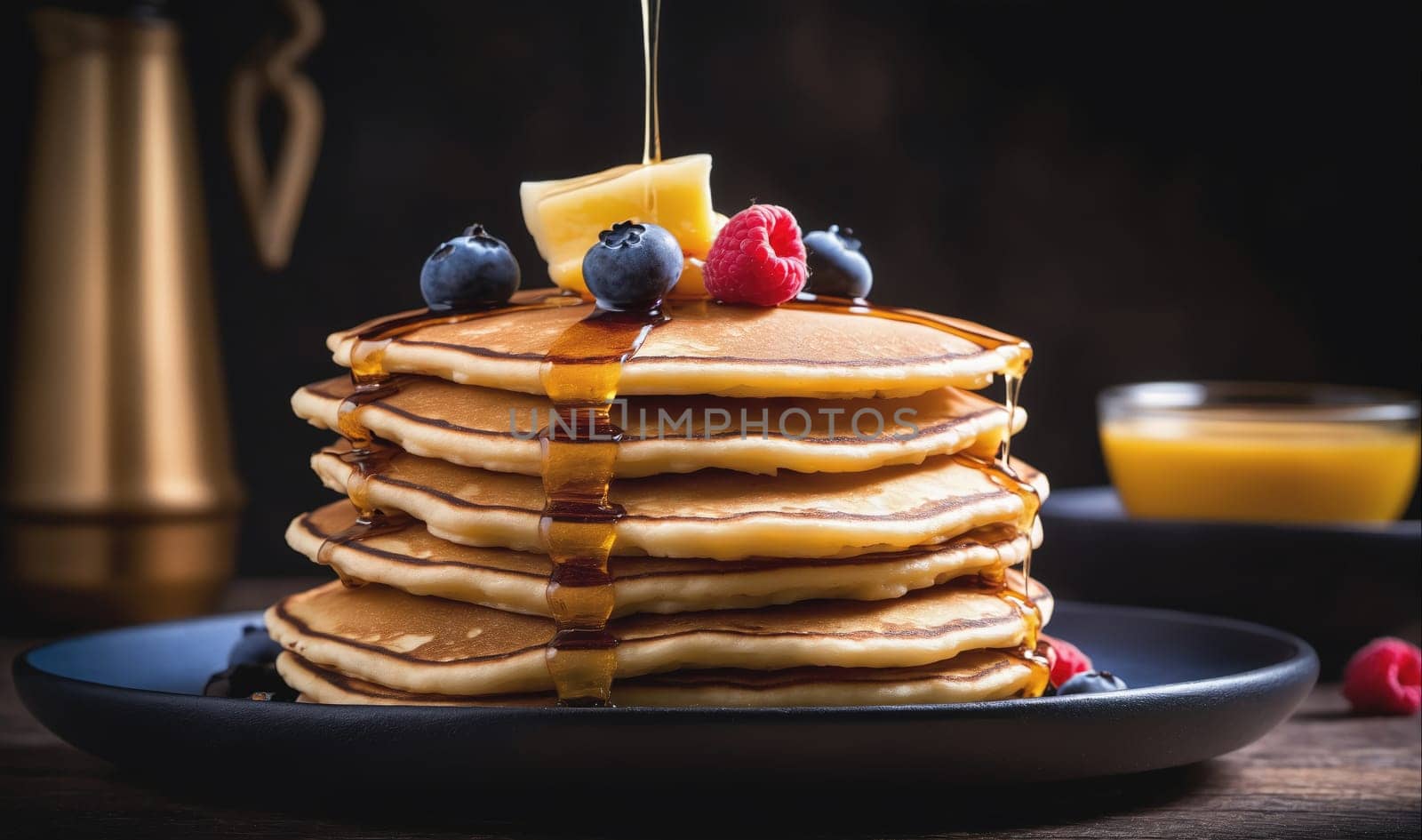 A stack of golden brown pancakes topped with blueberries, raspberries, and maple syrup sits on a blue plate on a wooden table. There is a small bowl of maple syrup in the background.