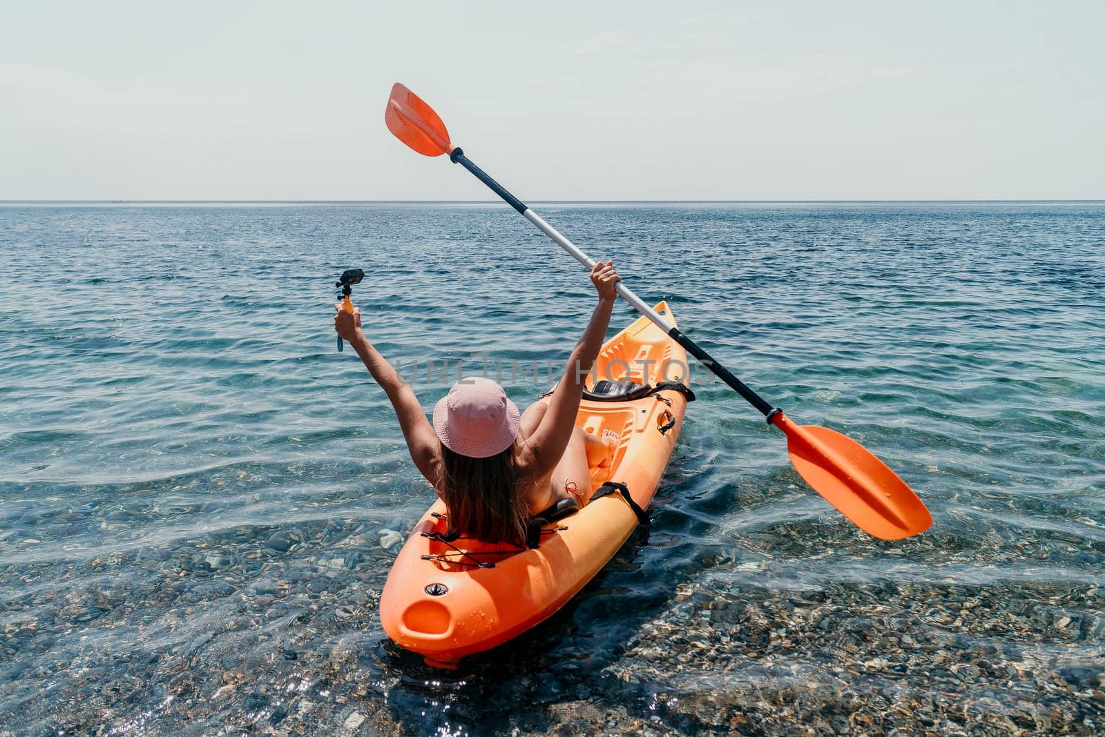 Happy smiling woman in kayak on ocean, paddling with wooden oar. Calm sea water and horizon in background