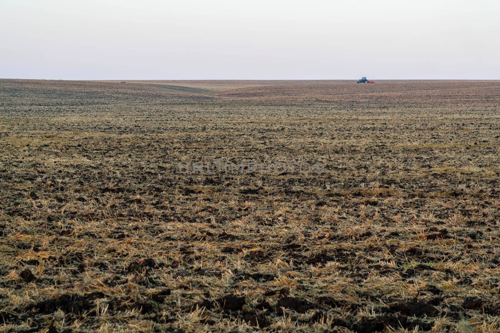 A tractor works diligently on expansive farmland, tilling the soil as the early morning light casts a soft glow. The landscape stretches endlessly, showcasing the open fields.