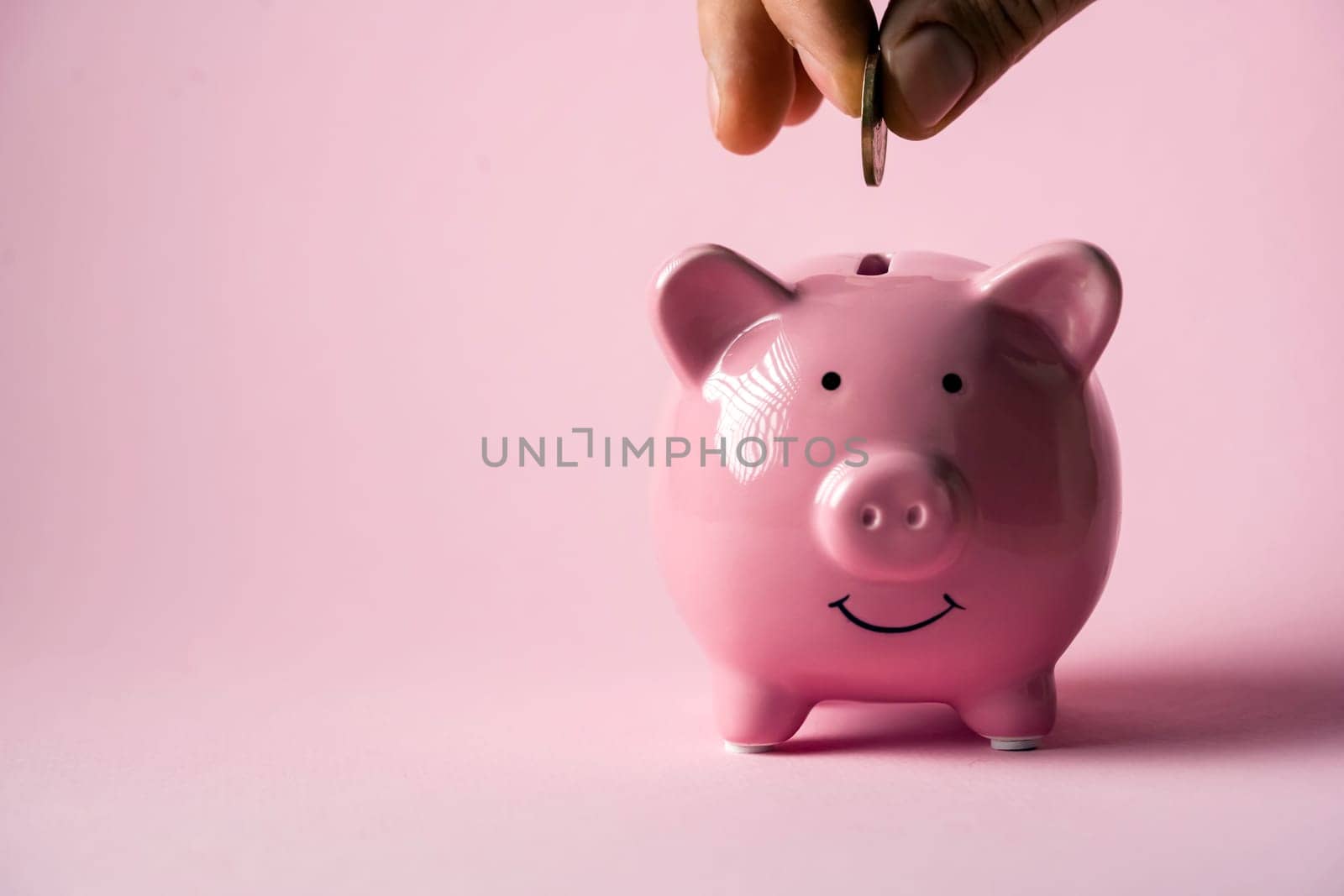 The hand holds a coin and puts it in a piggy bank to preserve wealth, savings and financial success.