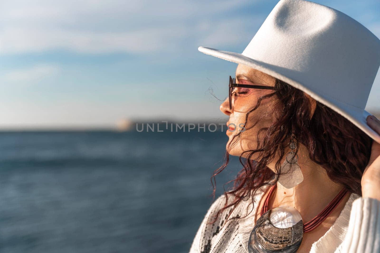 Portrait of a curly haired woman in a white hat and glasses on the background of the sea